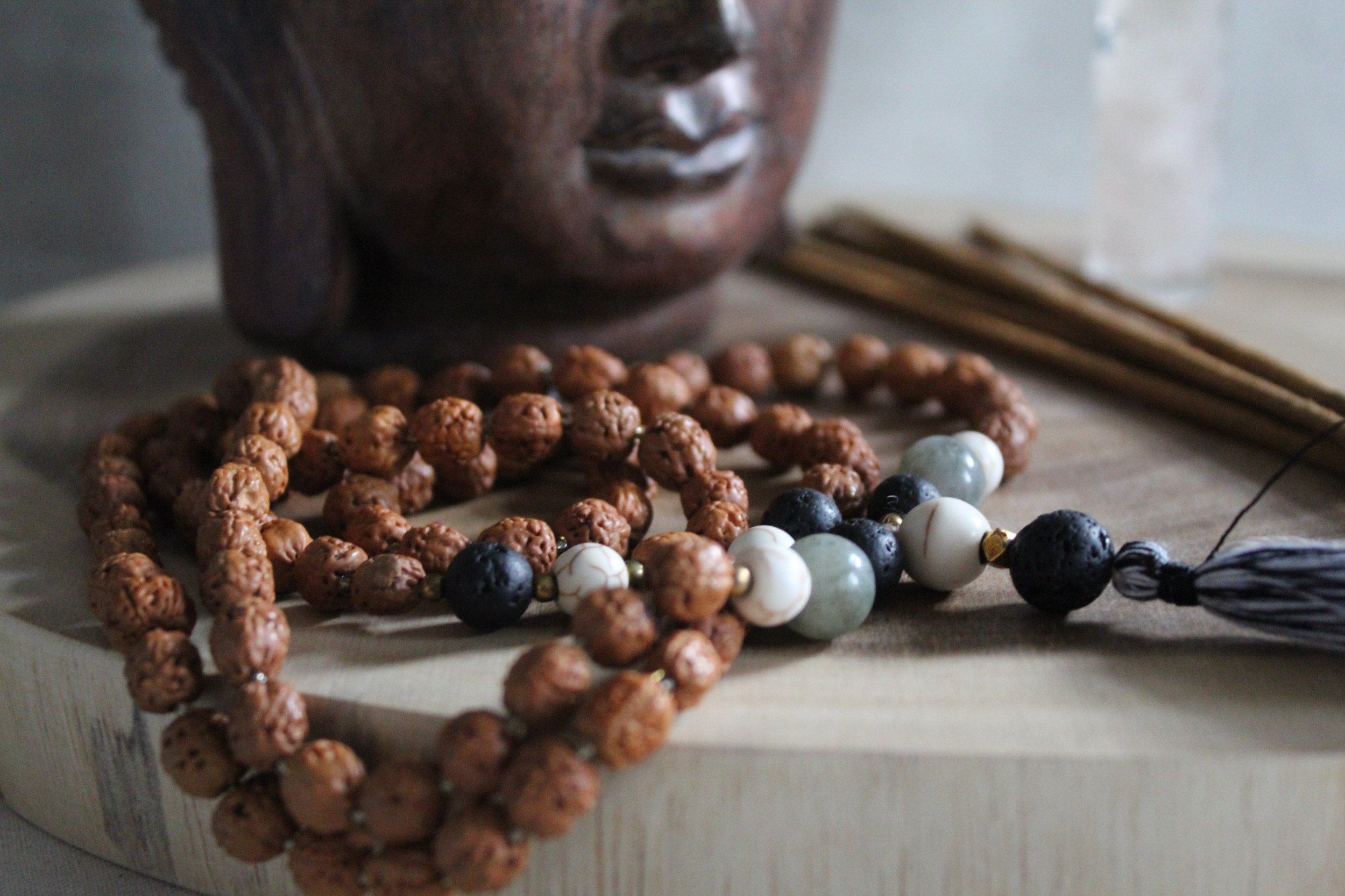 Close-up of Buddhist prayer beads resting on a wooden surface, with a carved wooden Buddha head in the background.