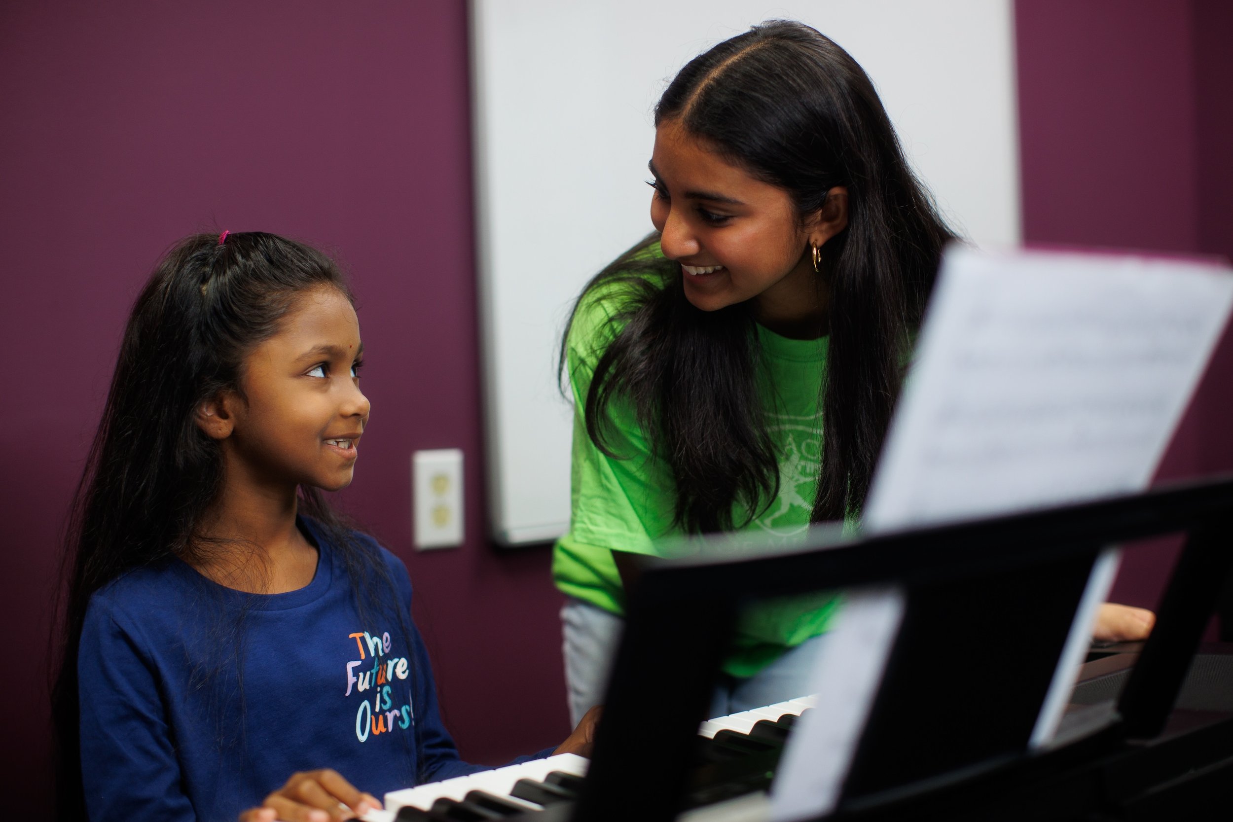 young student and teacher assistant smiling together at piano in classroom