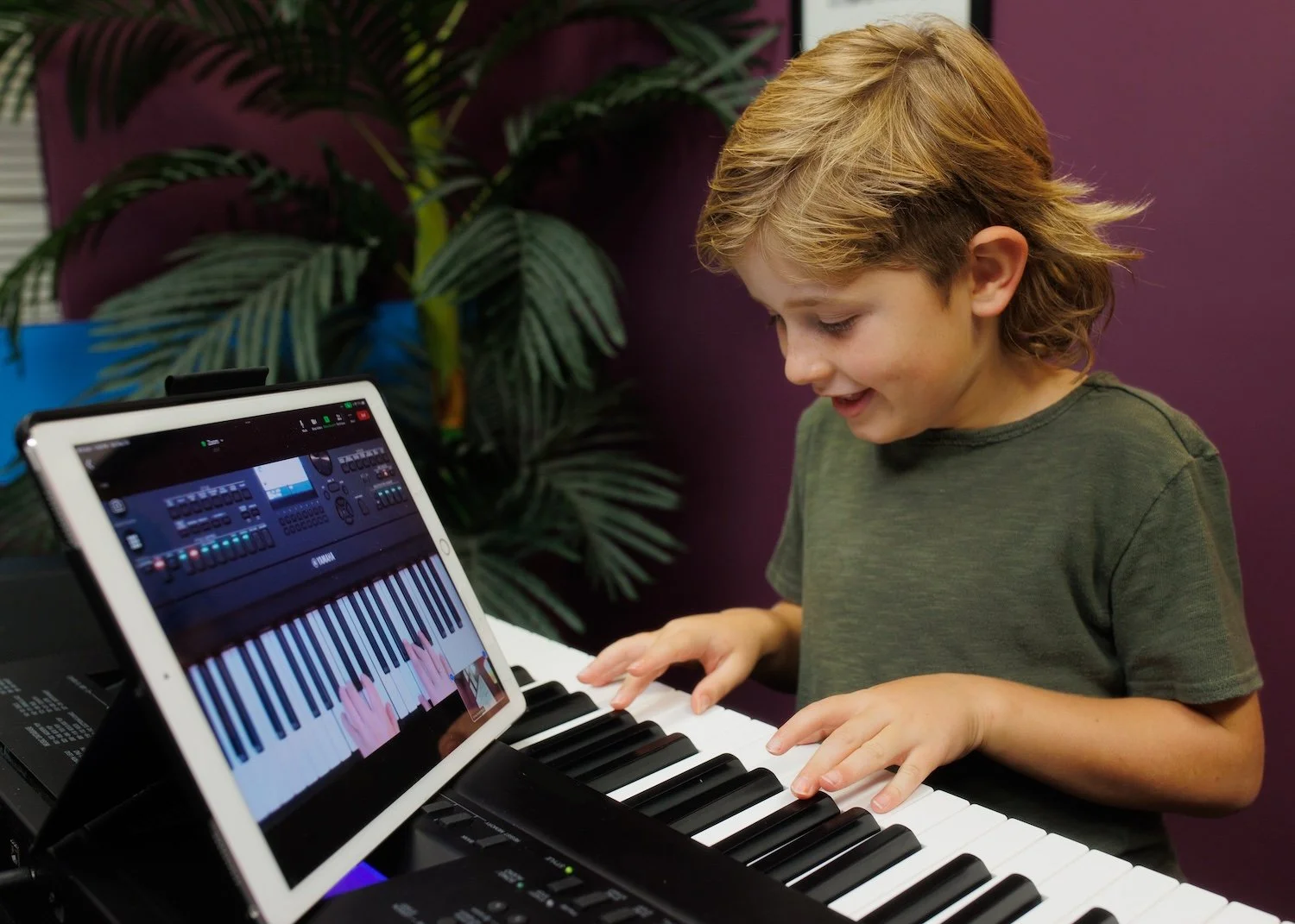 A young boy playing a keyboard piano, looking happy.