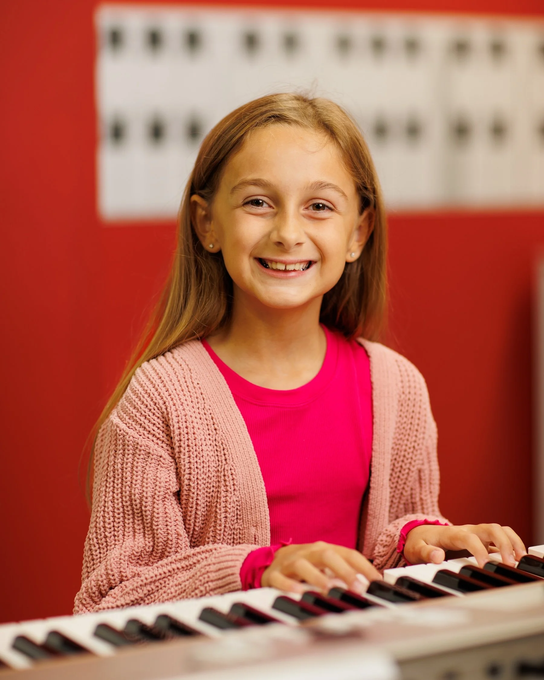 A young woman smiling, playing a keyboard in a music classroom