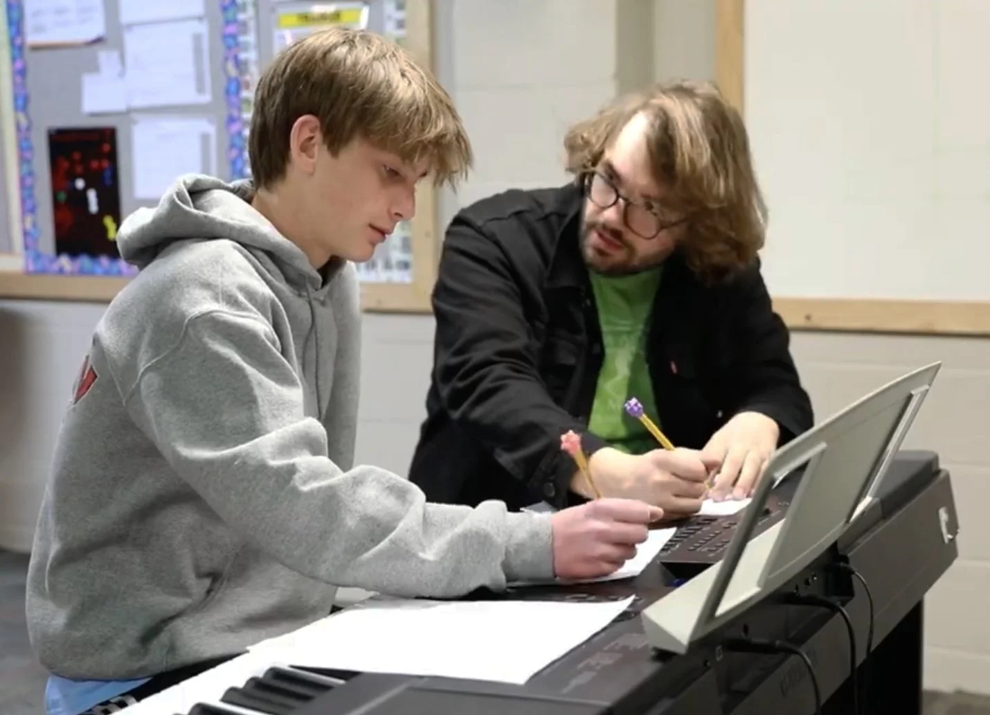 teacher with teen student writing music at piano