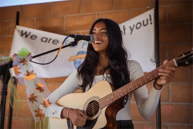 teen girl performing at outdoor concert with guitar and microphone