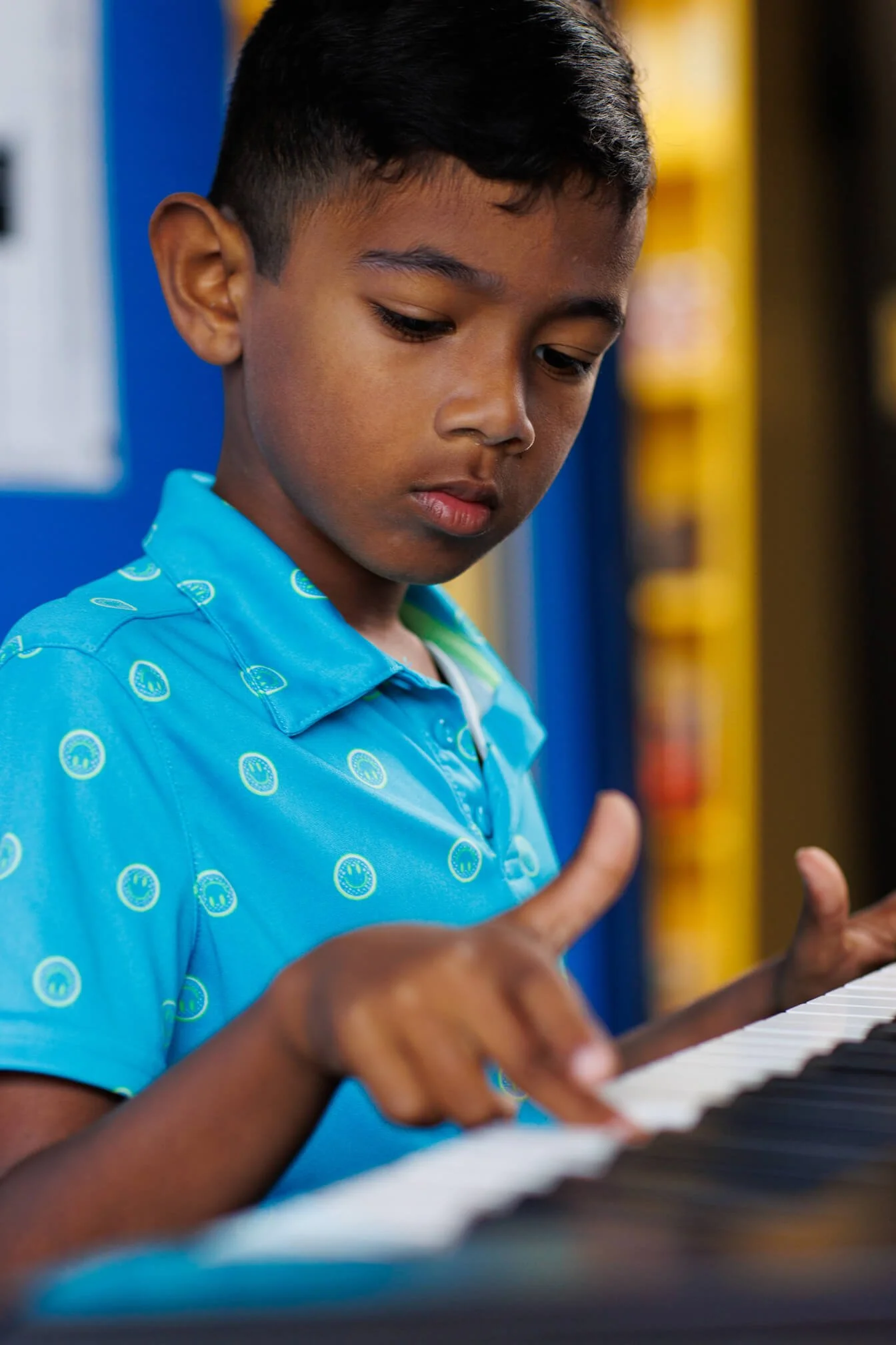 young student in blue shirt playing piano in classroom