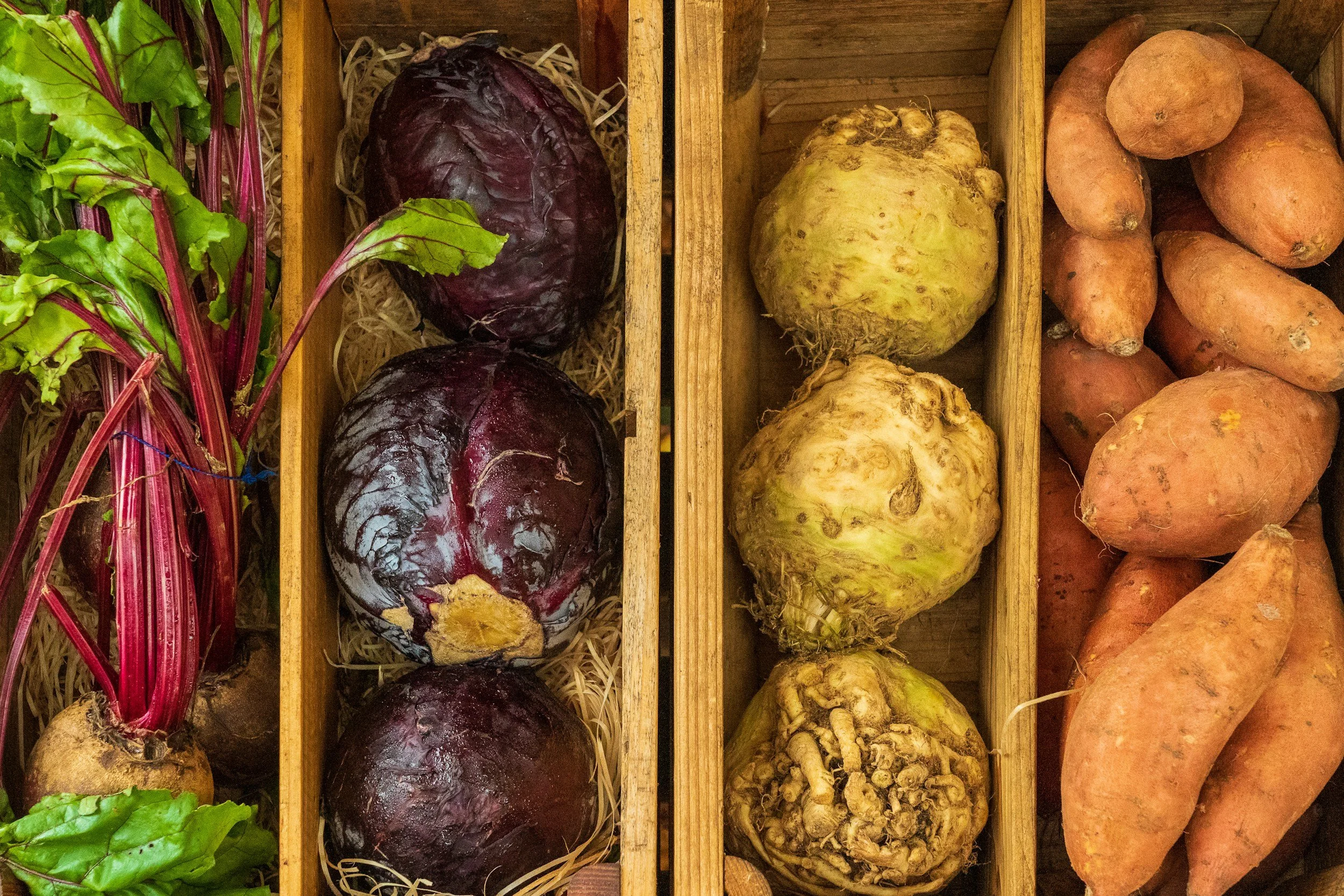 Fresh beets, celeriac, and sweet potatoes displayed in wooden crates.