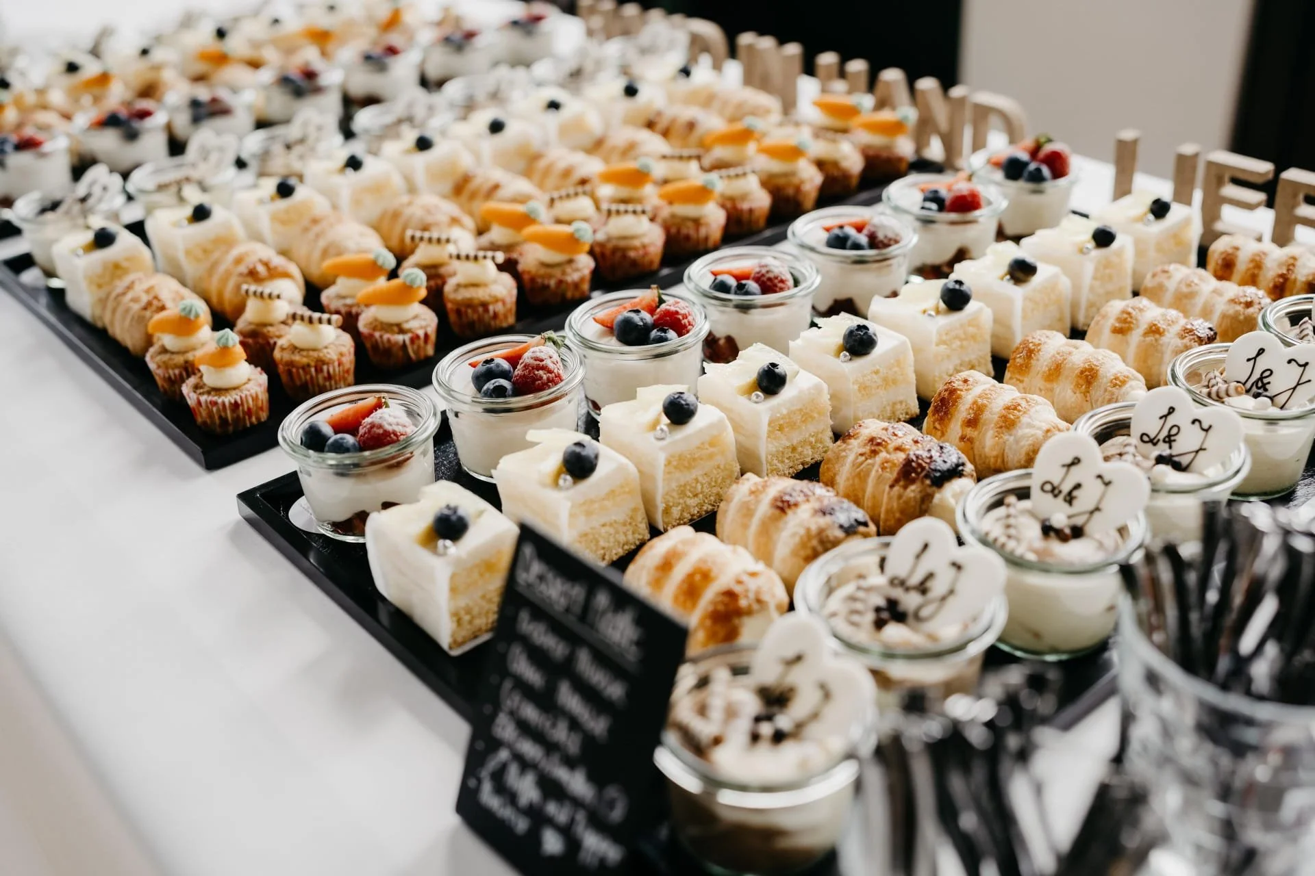 Verschiedene kleine Desserts und Cupcakes auf schwarzen Tabletts mit Beeren und Dekorationen