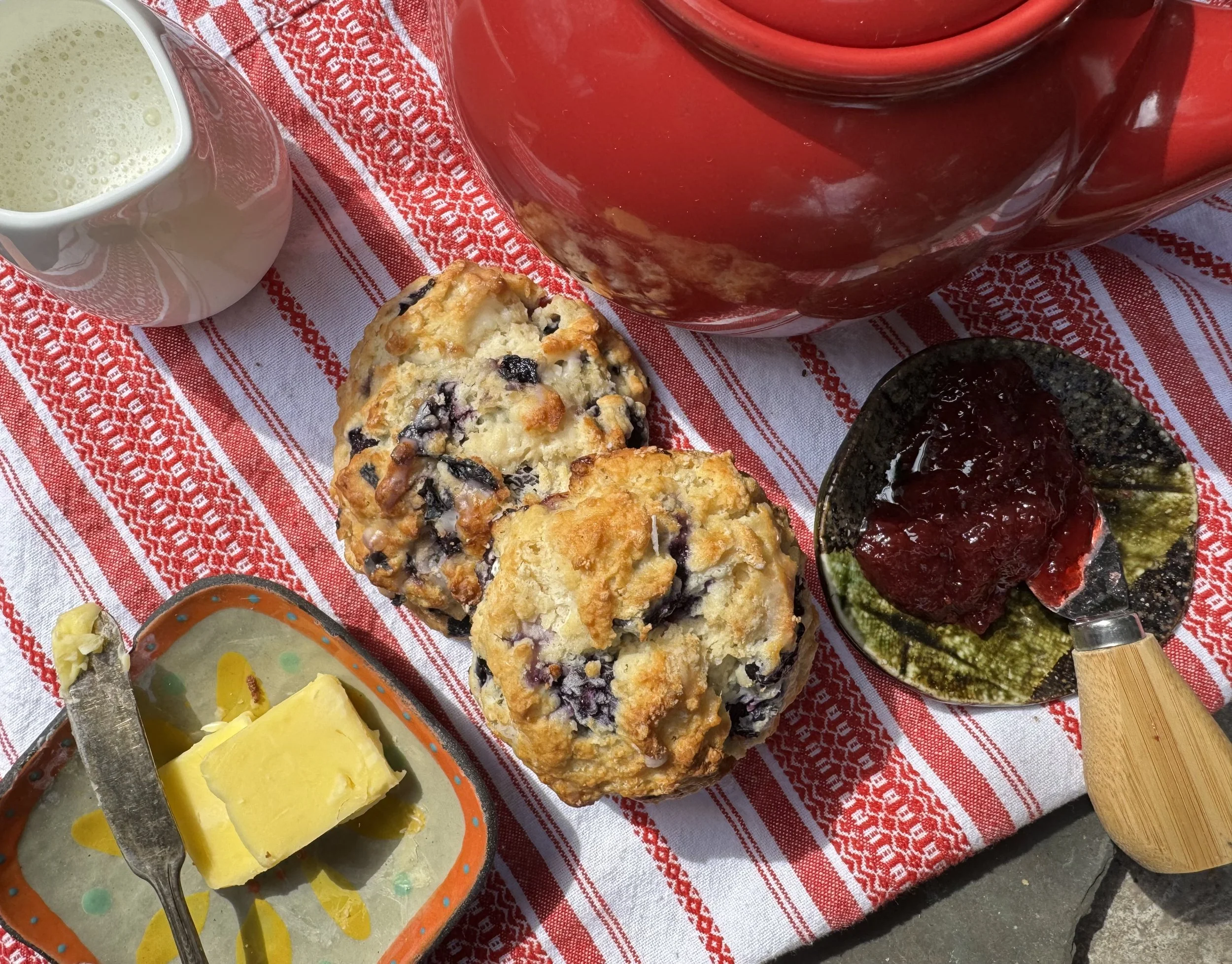 Two scones sit on top of a decorative table cloth with butter and jam next to it