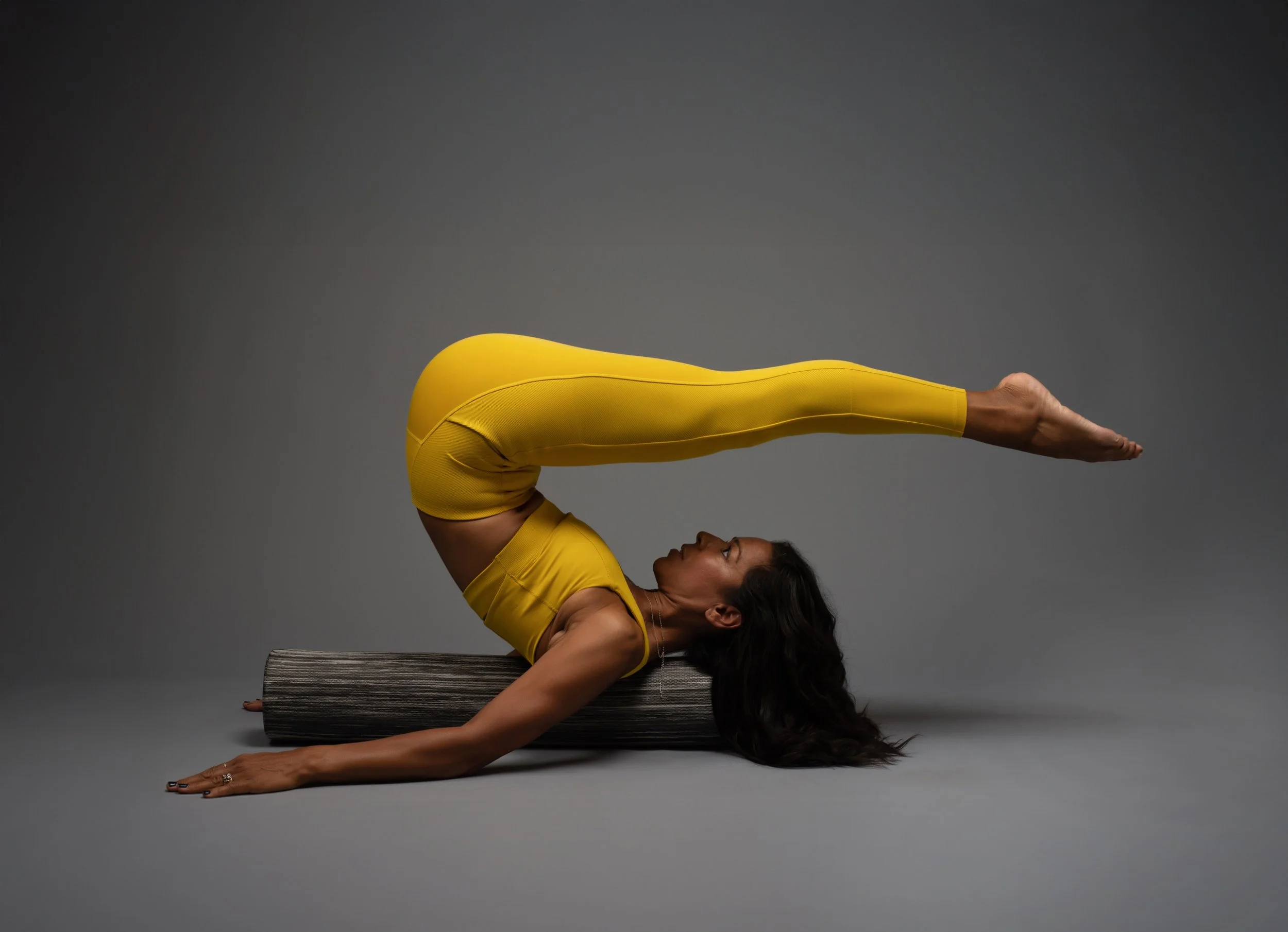 LaBriece practicing pilates on a gray background, wearing yellow activewear and using a Body Balanced roller
