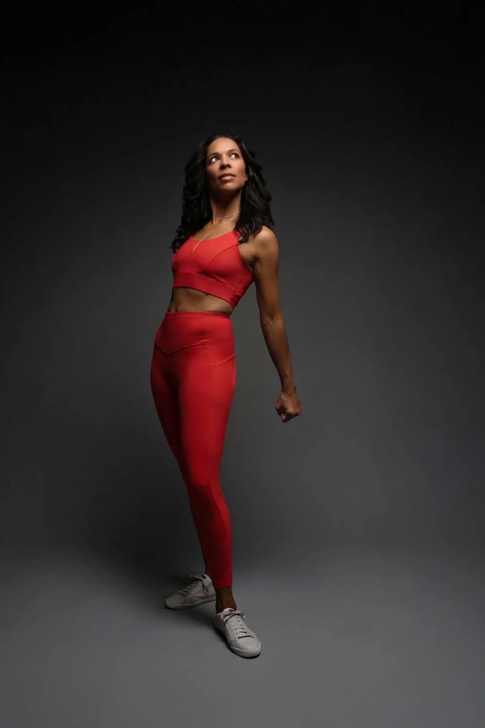 LaBriece standing against a dark background, wearing a red activewear, with white sneakers, and looking upwards.