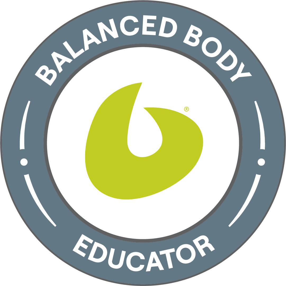 A circular badge with a gray outer ring and white text that reads 'BALANCED BODY EDUCATOR.' Inside the ring is a black circle with a green abstract symbol in the center.