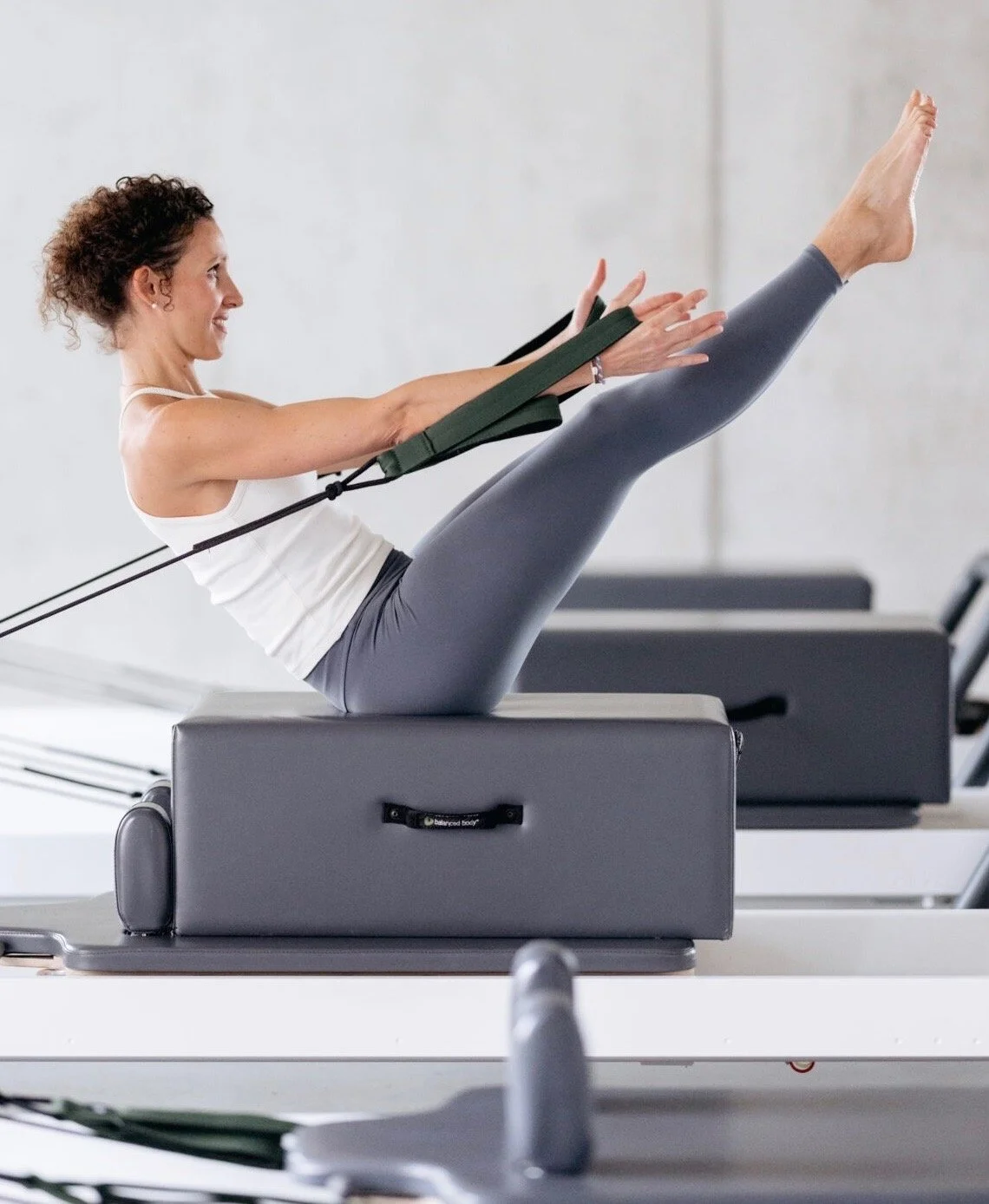 A woman exercising on Pilates reformer machine using resistance bands in a fitness studio.