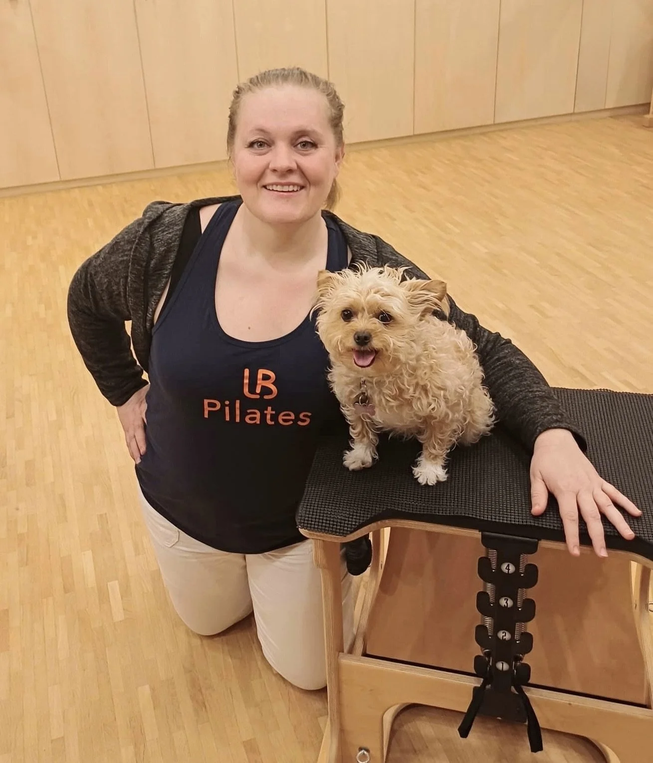 A woman kneeling on the floor smiling at the camera, wearing a navy tank top with
