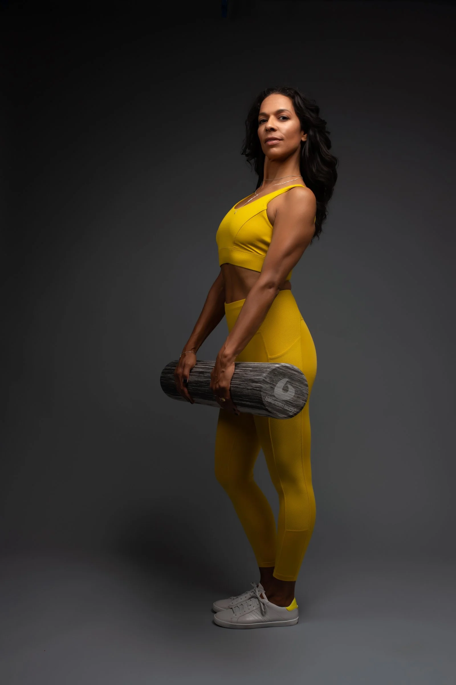 LaBriece in yellow workout attire holding a foam roller and standing against a dark background.