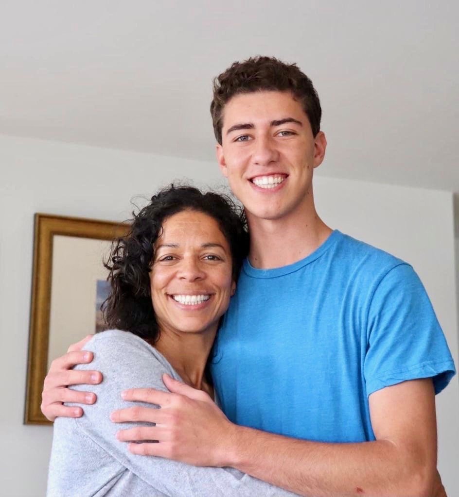 LaBriece and her son hugging and smiling at the camera inside a home, with a framed picture on the wall behind them.