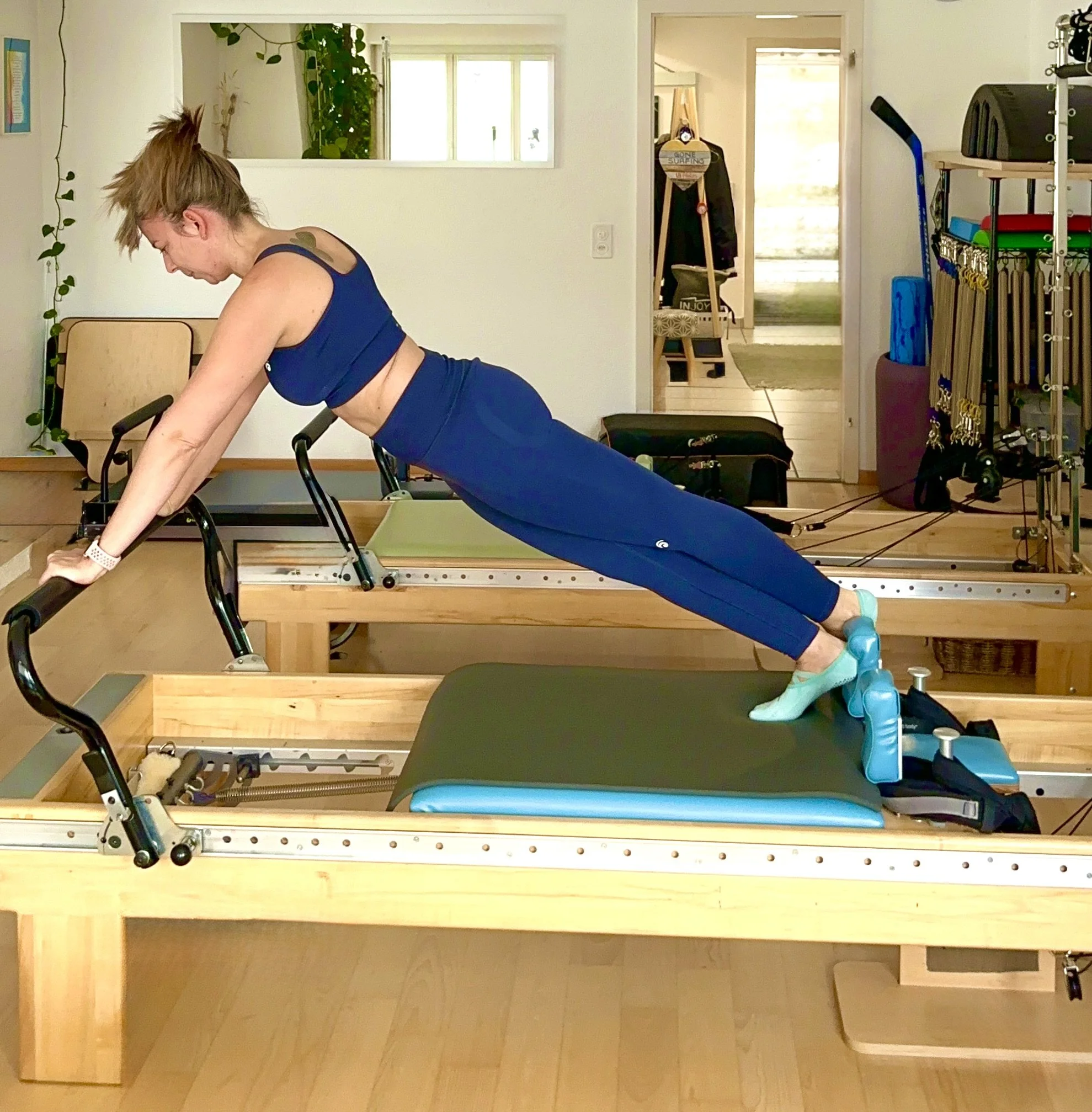 Woman doing Pilates on a reformer machine in a home fitness studio.