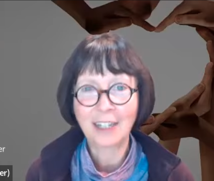 A woman with short brown hair and glasses smiling, with hands forming a heart shape above her head.