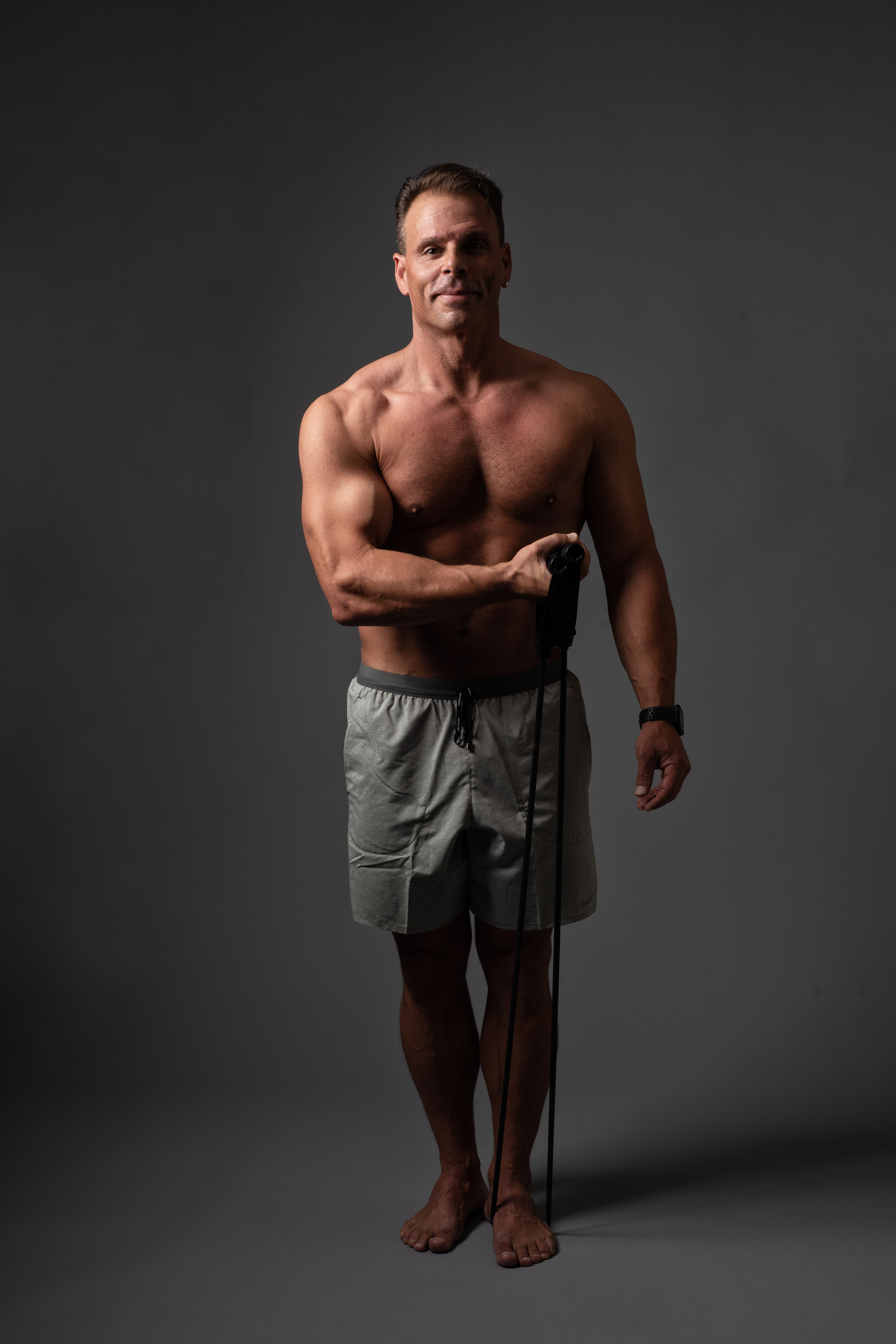 Patrick standing barefoot on a gray background, wearing gray shorts and holding a jump rope in one hand.