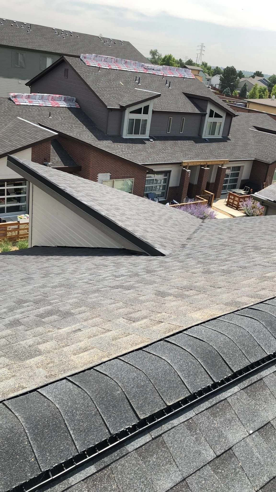 View of multiple houses with gray shingle roofs, some with solar panel installations, and a cloudy sky in the background.