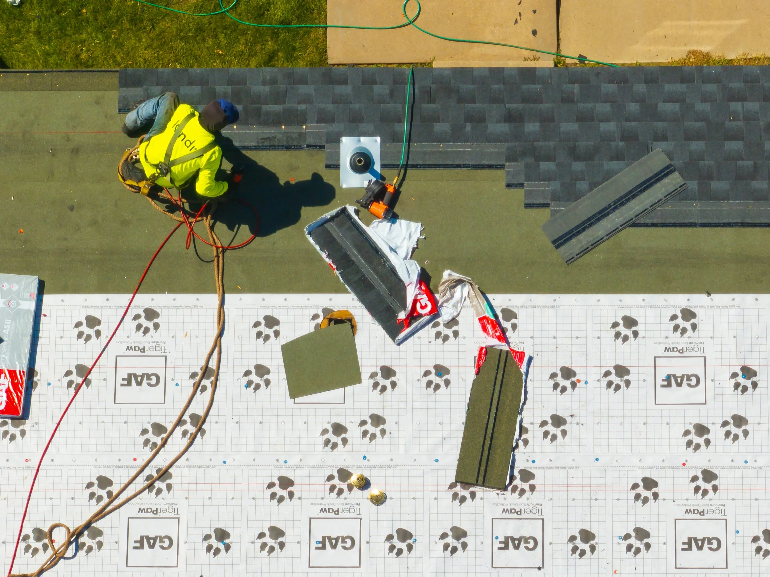 Construction worker in a yellow jacket working on roofing, laying down insulation panels with a grid pattern and paw print design.