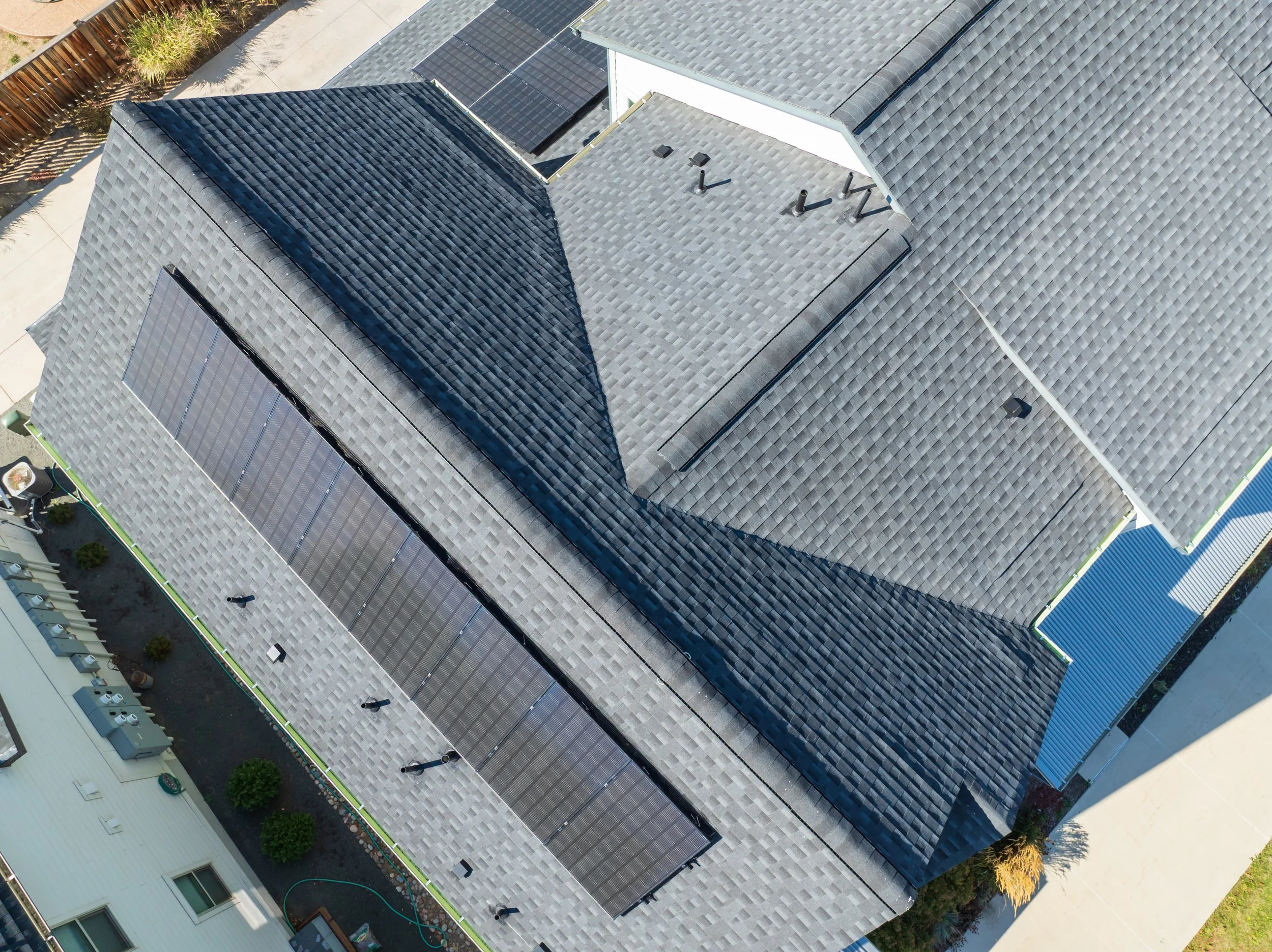 An aerial view of multiple house roofs with solar panels installed on a gray shingled roof.