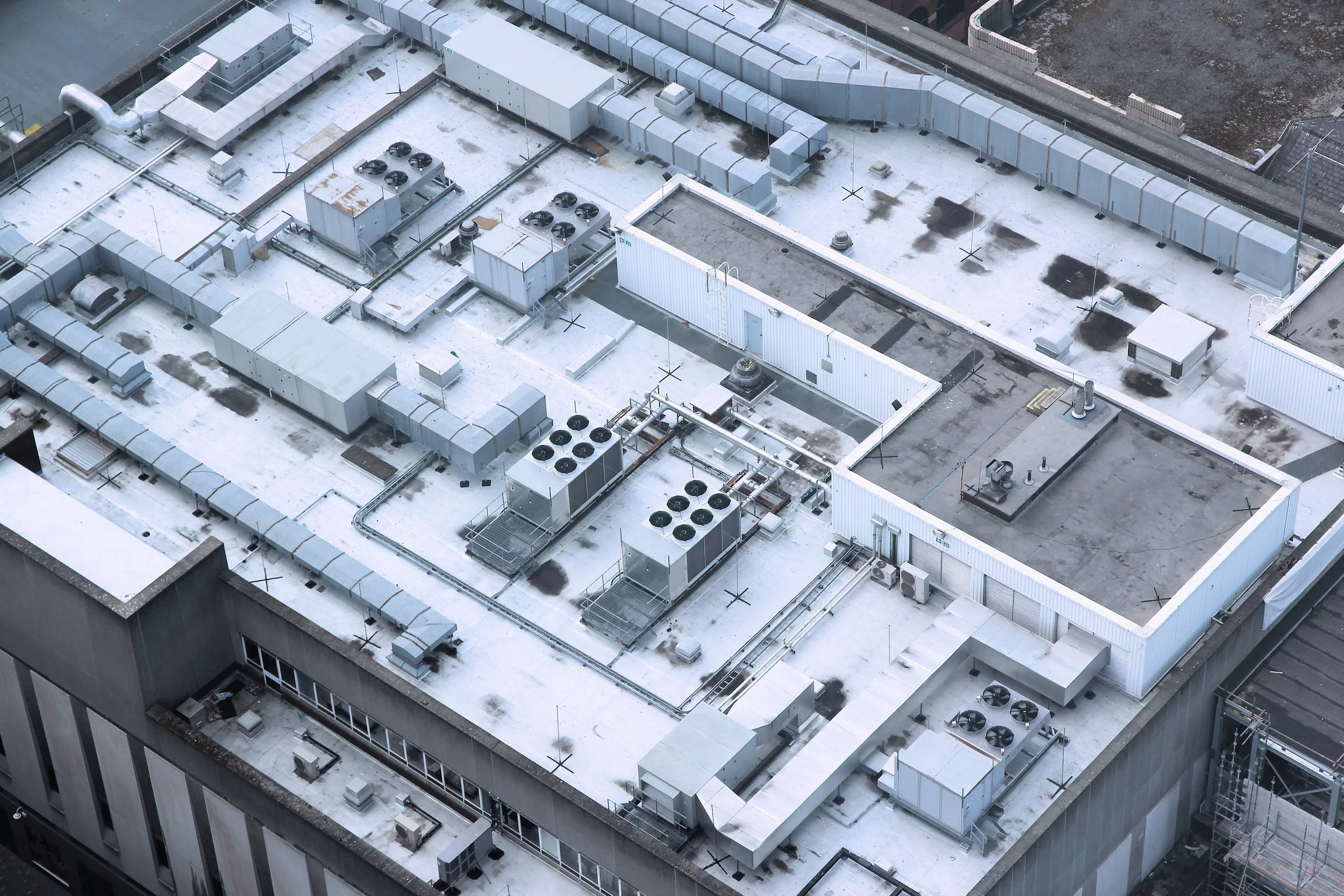 Aerial view of a commercial building's rooftop featuring HVAC units, ventilation ducts, and other mechanical equipment on a flat, white surface.