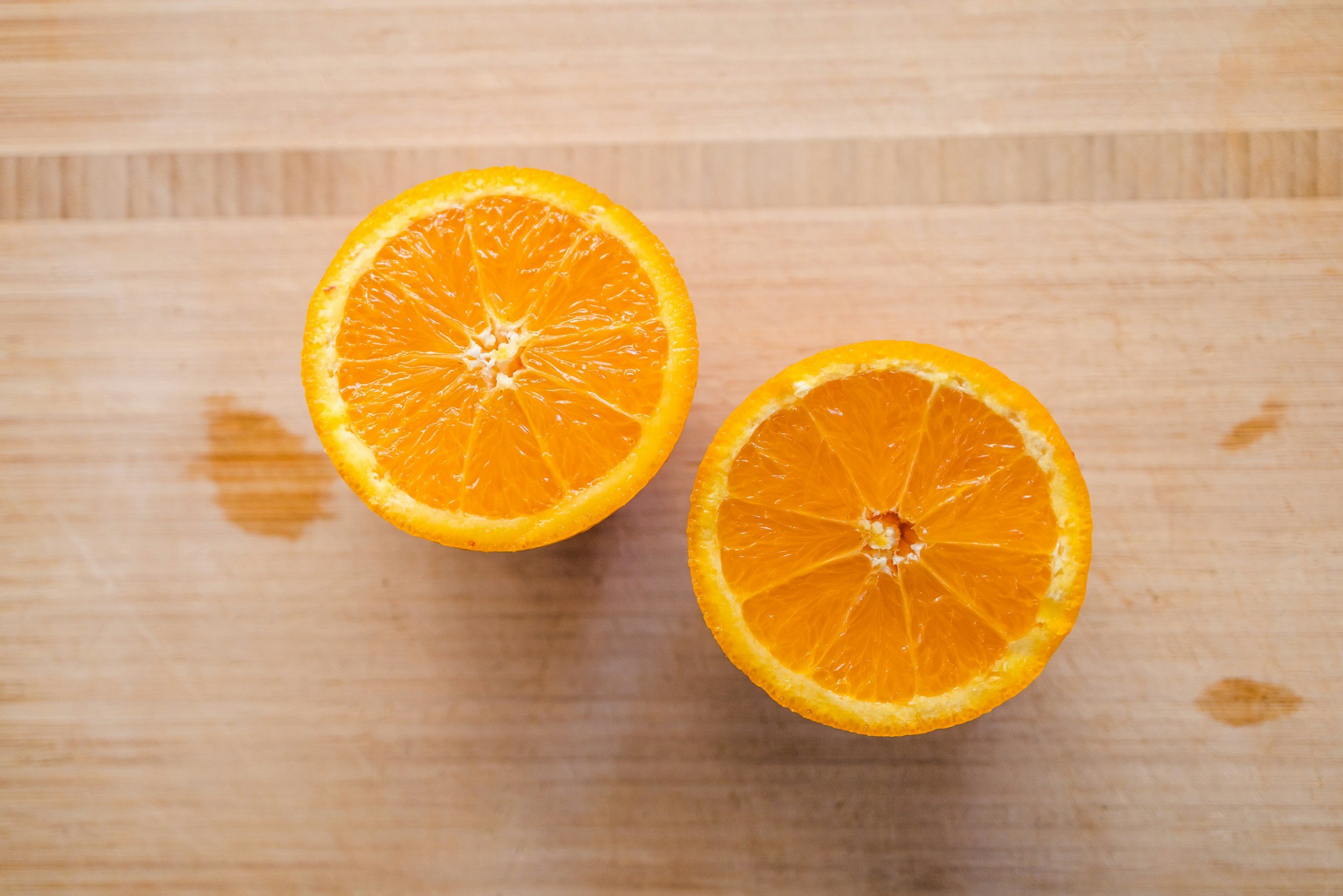 Two halves of an orange on a wooden cutting board.