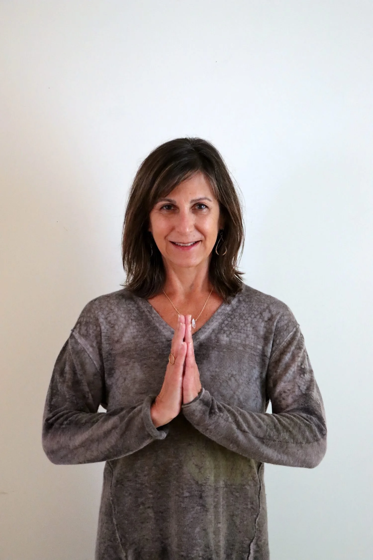 A woman stands in front of a beige wall with her hands together