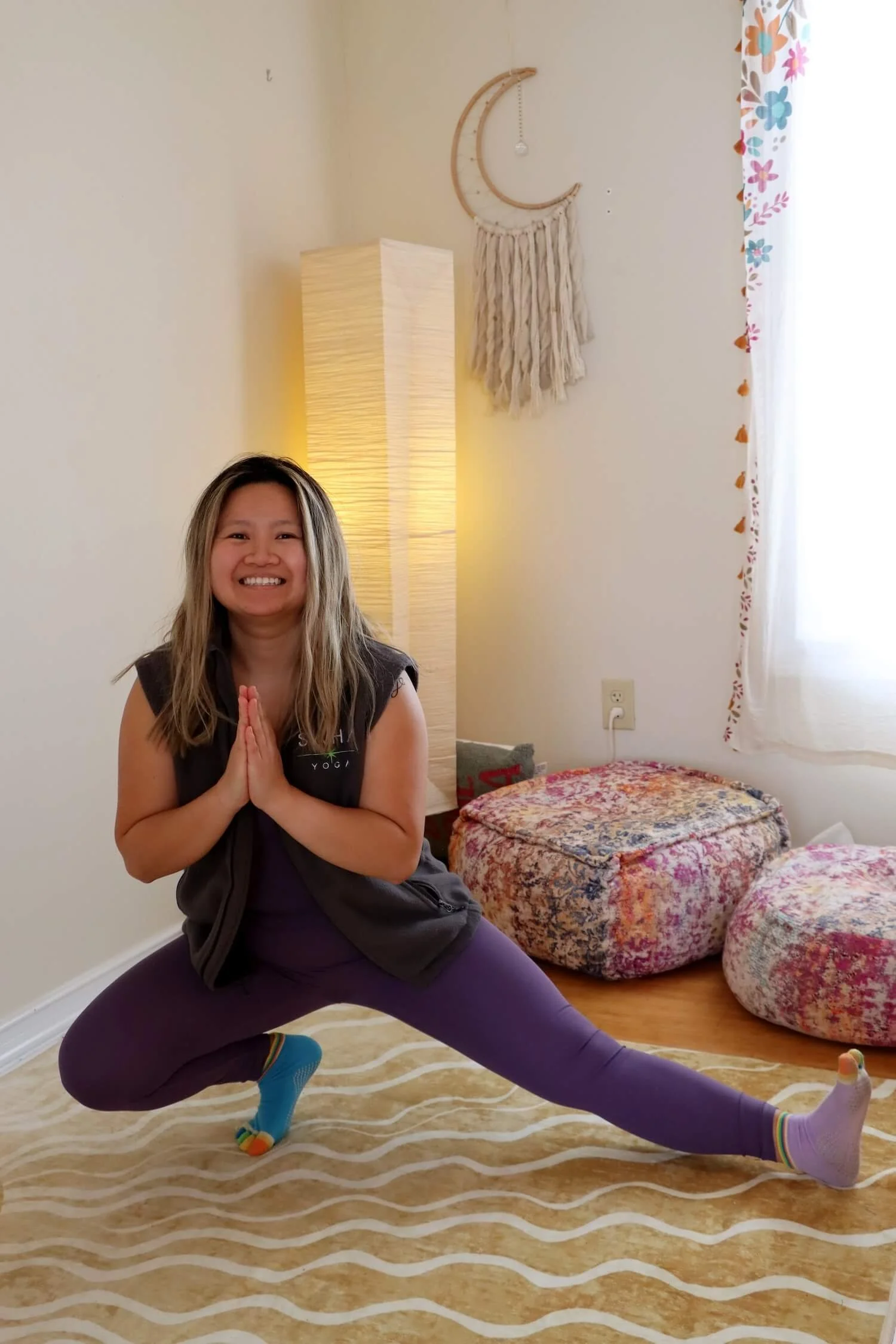 A smiling woman in a yoga pose with bolsters behind her
