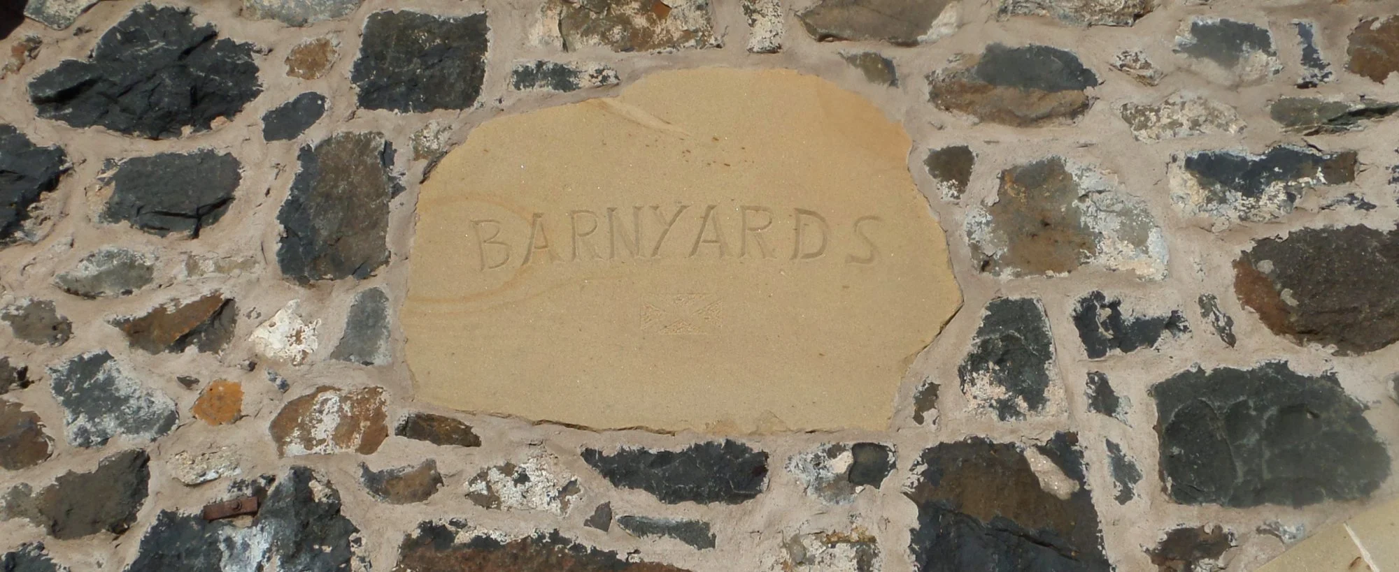 A stone wall with a beige engraved plaque that reads 'BARNYARDS' in the center.