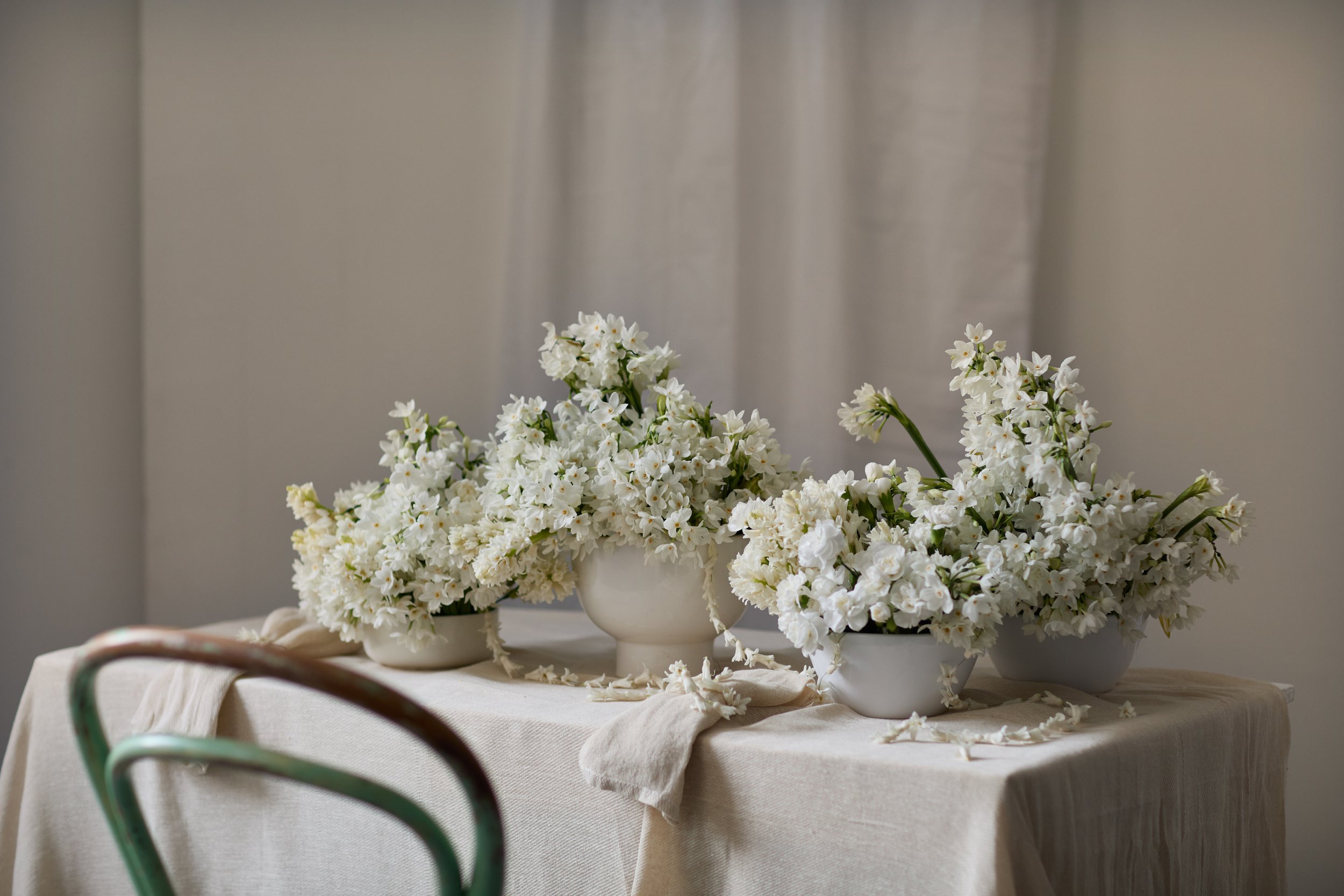 White flowers arranged in white vases on a table with a beige tablecloth.
