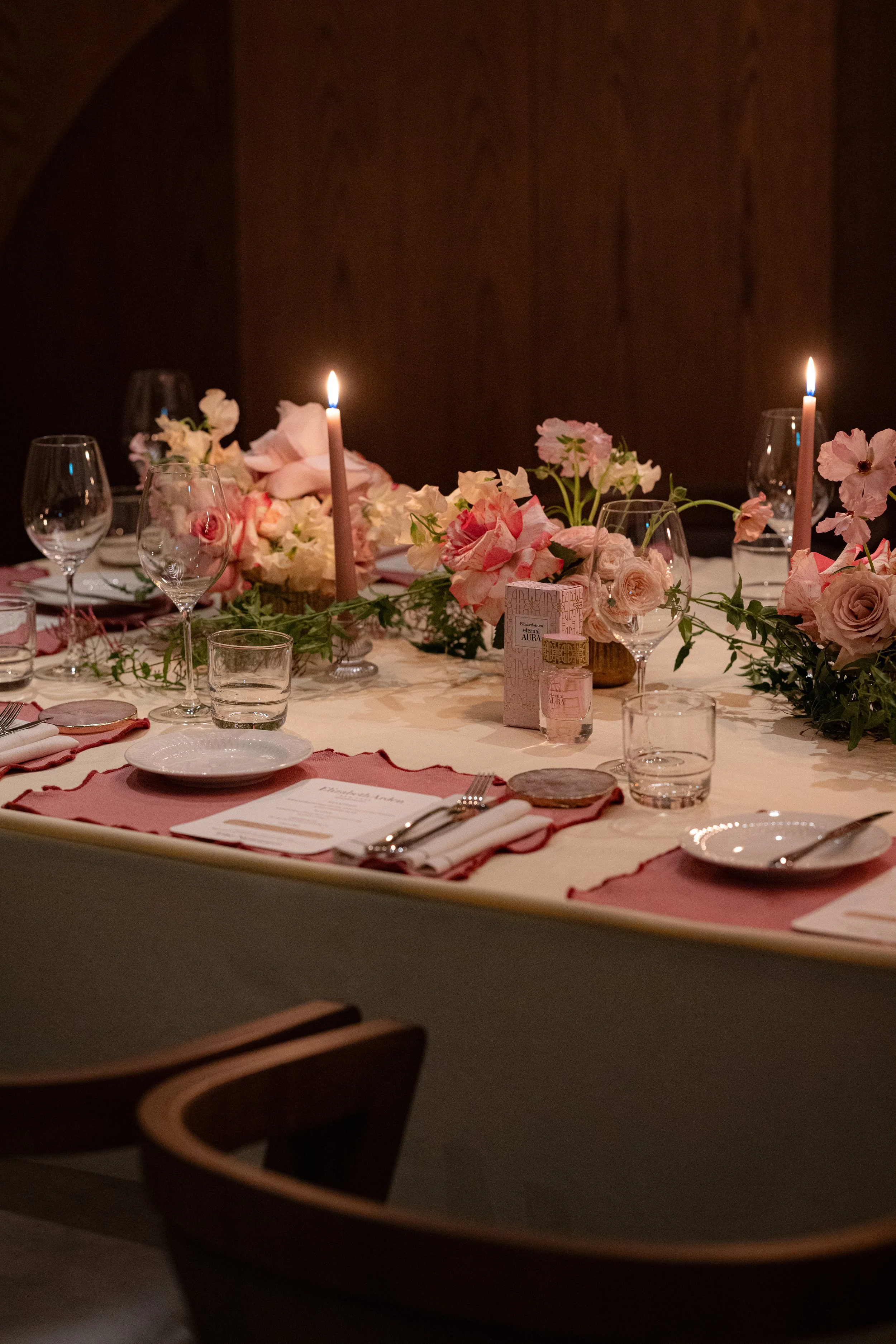 A decorated dining table with pink candles, flowers, glassware, and a menu, set for a special occasion or dinner.