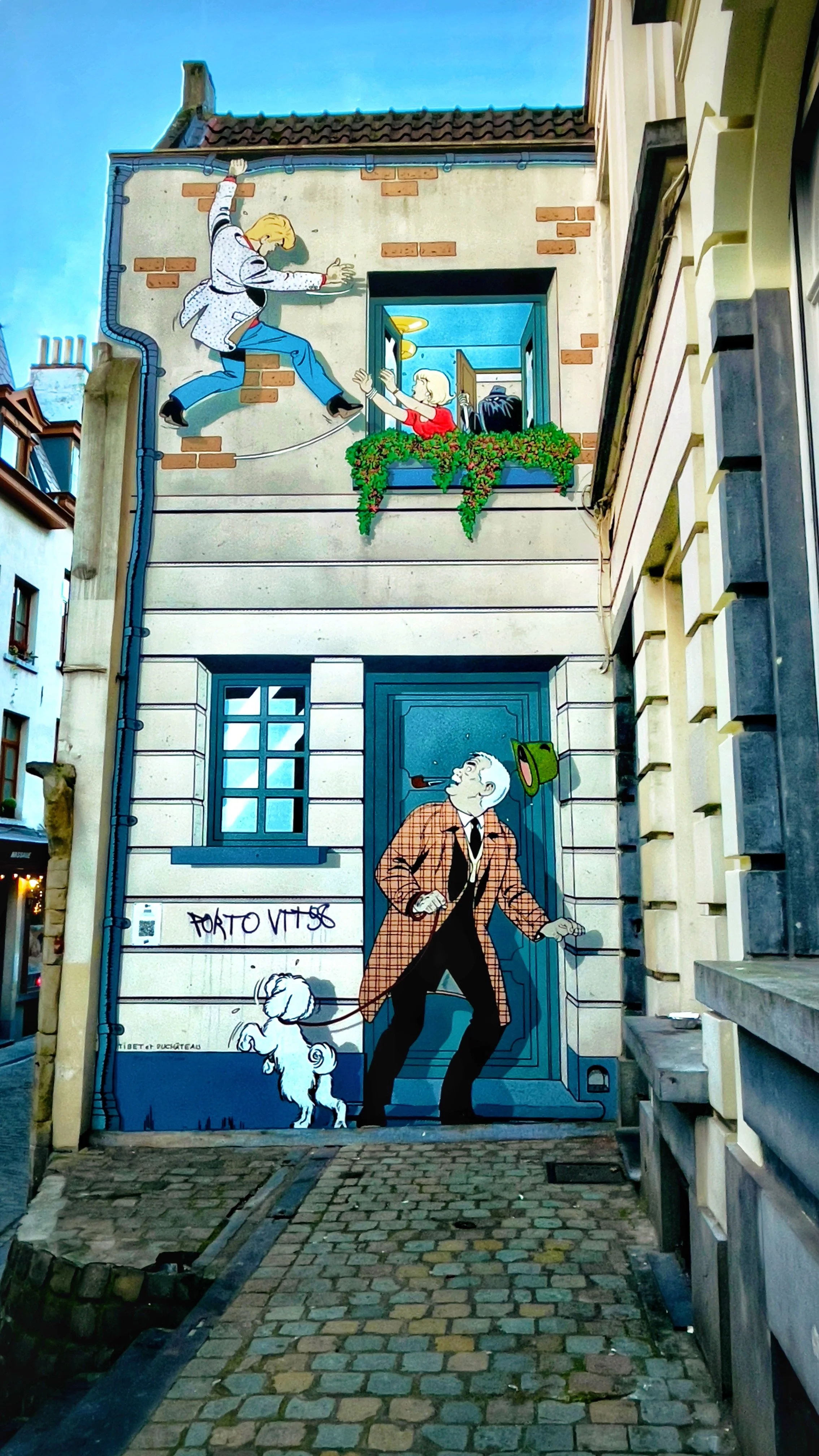 Street art mural depicting a man walking a dog in front of a building, with a scene of a woman reaching out to a man climbing up a wall painted above, who appears to be hanging from a rope and reaching toward her.