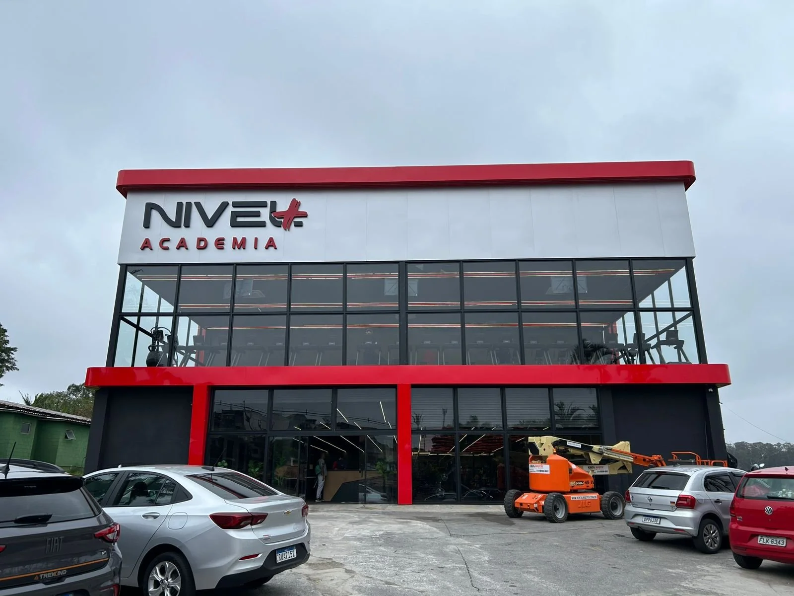 Desenho técnico de um projeto de arquitetura de uma casa moderna, com anotações e detalhes feitos à mão por uma pessoa usando uma caneta, sobre uma imagem de uma construção real ao fundo.