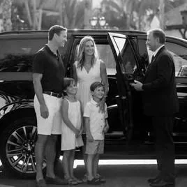 A family standing outside near a car, greeting a man in a suit.