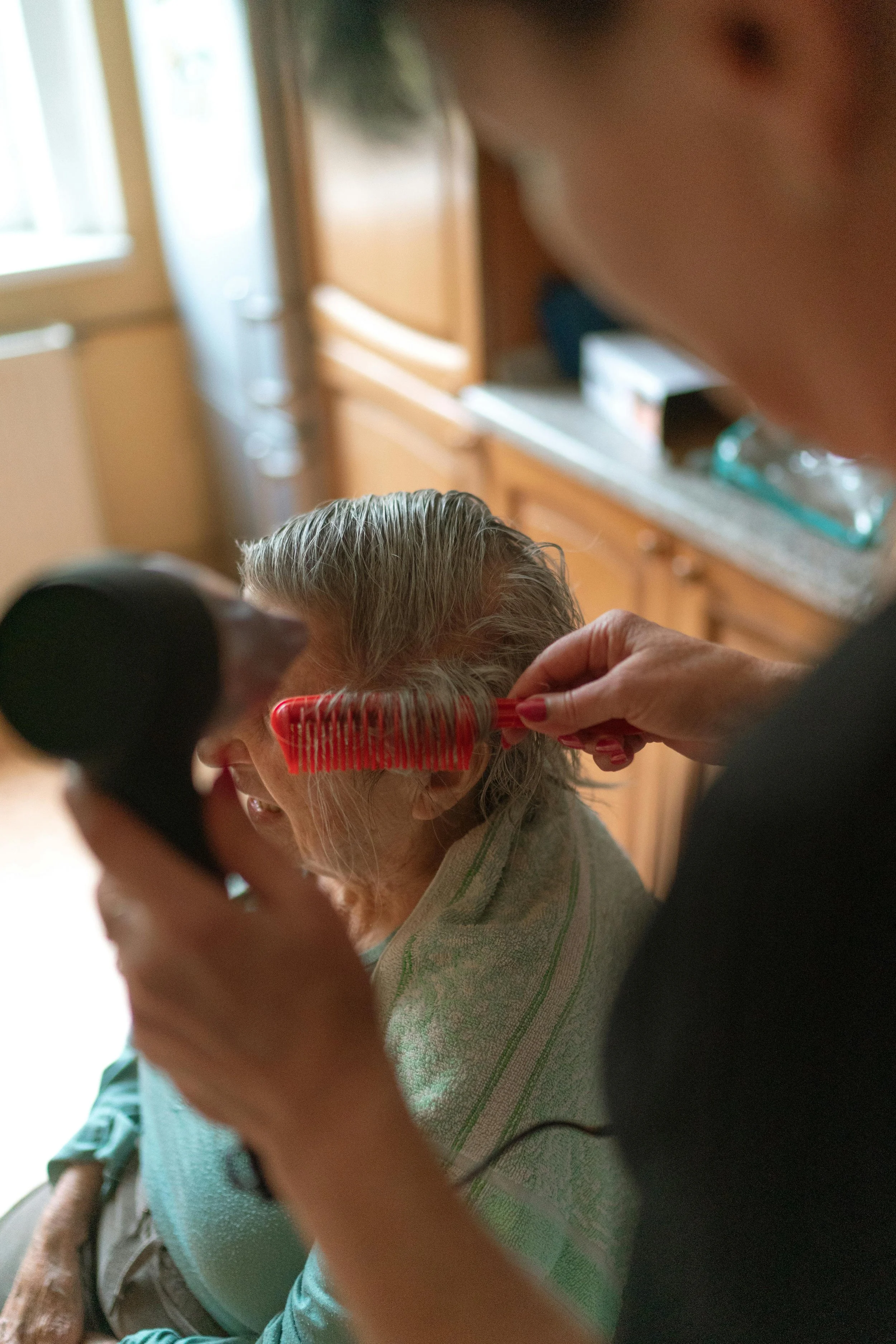 Une femme âgée se lave les mains dans une salle de bain moderne avec des murs en carrelage blanc et des accessoires en verre.