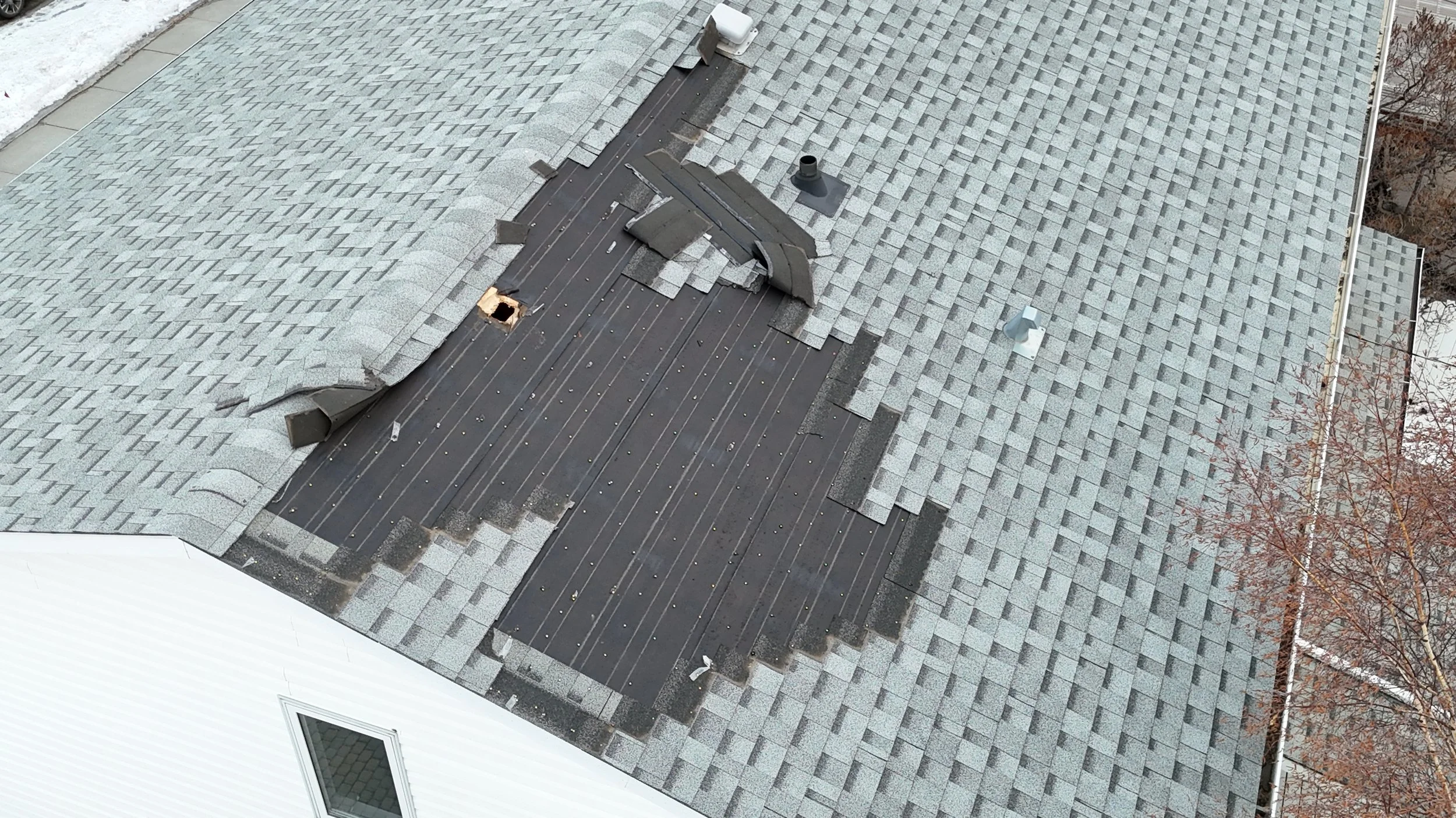 A rooftop with gray shingles, with a missing shingle due to a windstorm.
