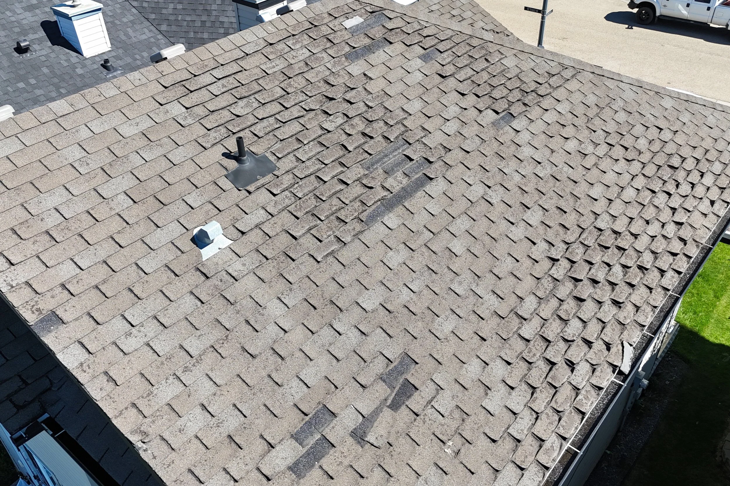 An aerial view of a house roof with brown shingles, which has signs that it needs new shingles.