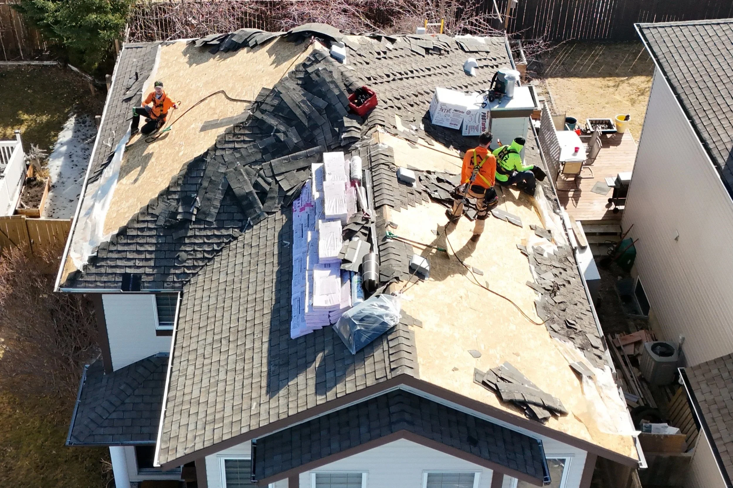 Aerial view of a house with a partially reroofed section, showing roofers working on removing old shingles and installing new roofing materials.