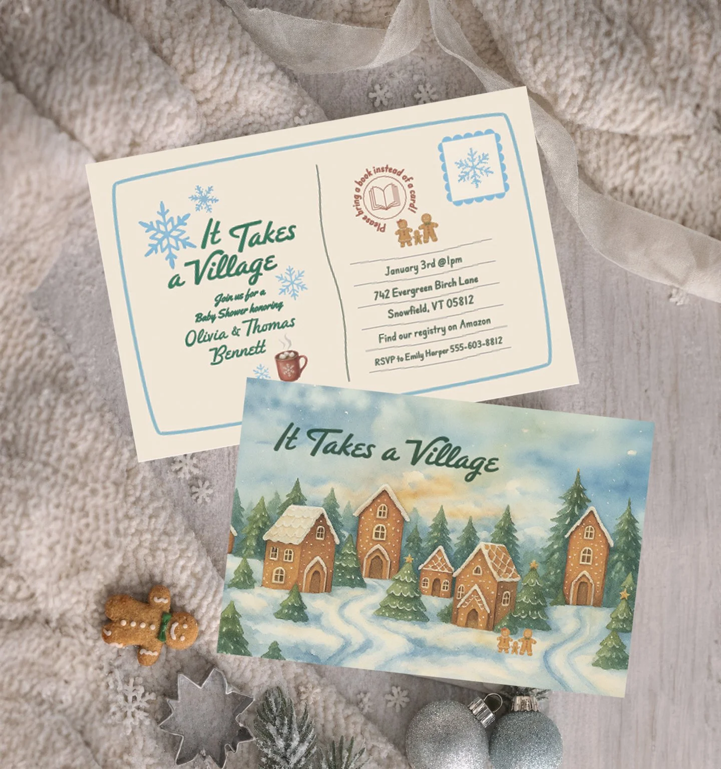 A  invitation for a baby shower with the title 'It Takes a Village', showing the date January 3rd, location in Snowfield, VT, and RSVP details. The invitation features a snowy village illustration with gingerbread houses and trees. There are holiday decorations around, including a gingerbread man, silver ornaments, snowflake cutouts, and evergreen branches.