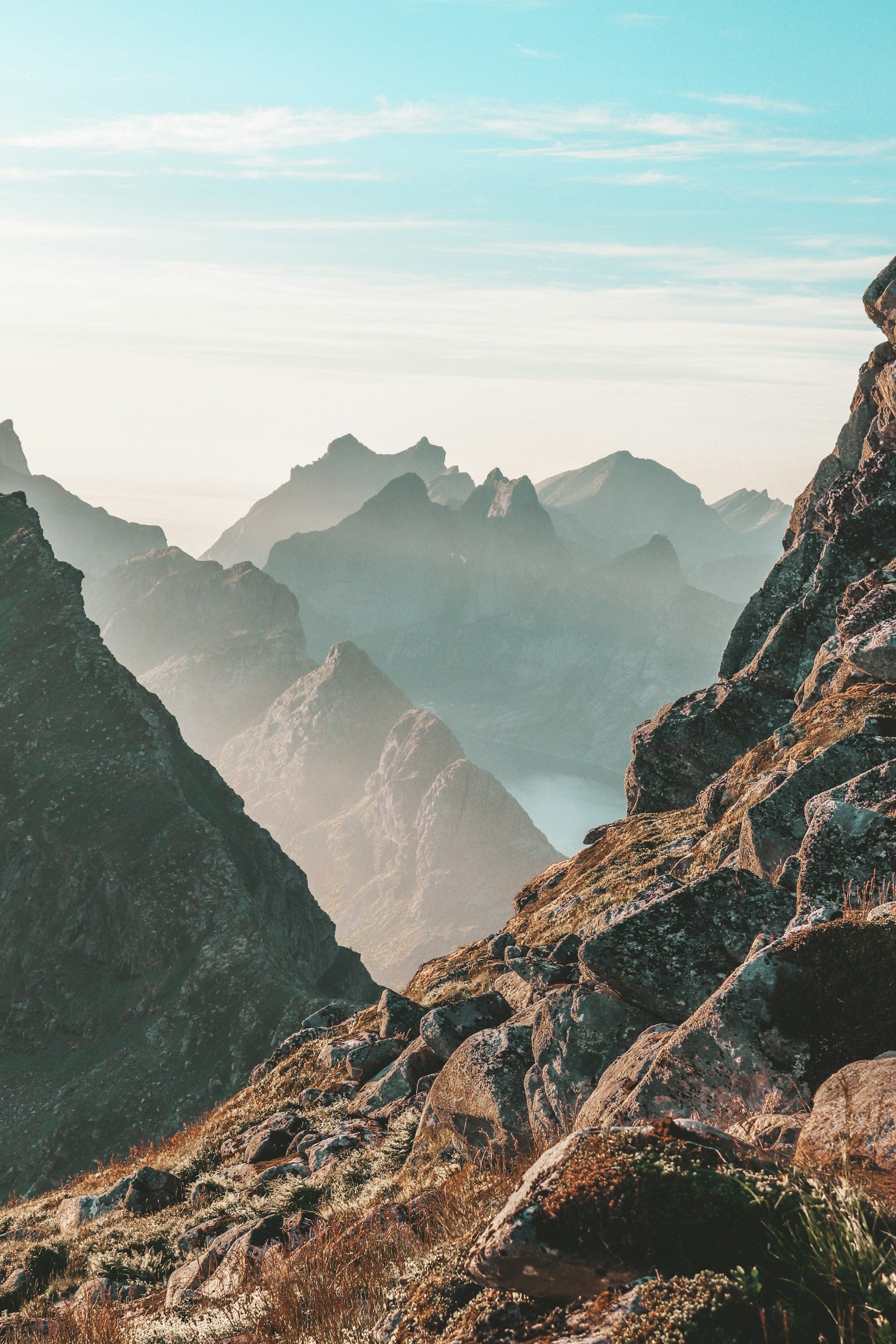 Mountain landscape with rocky peaks, distant mountain ranges, and a light sky.
