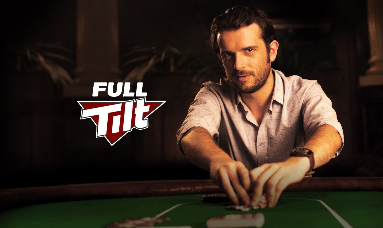A man with dark hair and beard sitting at a poker table, holding poker chips, with a serious expression, in a dimly lit room.