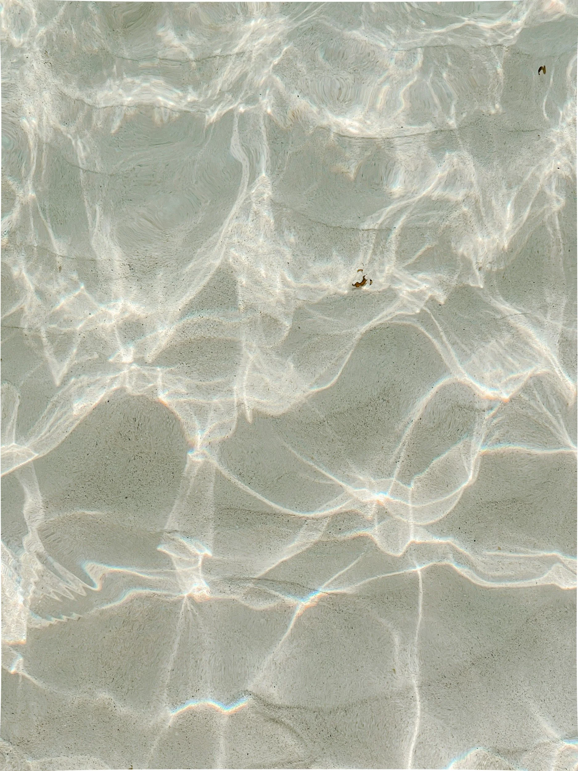 Close-up of sunlight reflections on a sandy beach underwater.