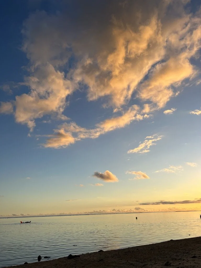 Coucher de soleil sur la mer avec des nuages oranges et roses dans le ciel et un rivage sableux à l'avant-plan.