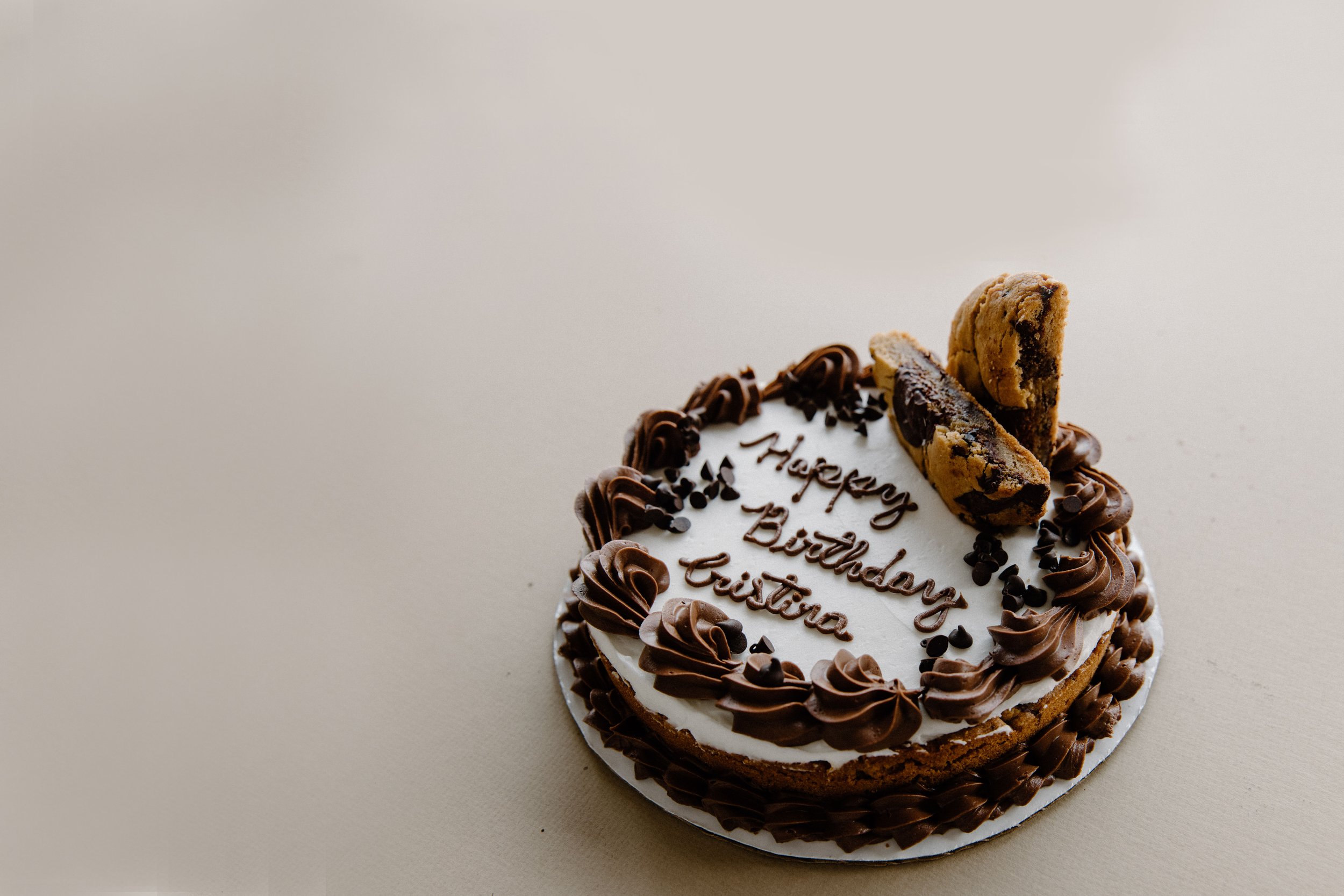 Chocolate and vanilla birthday cake with chocolate frosting and cookies on top, decorated with chocolate sprinkles and writing that says 'Happy Birthday'.