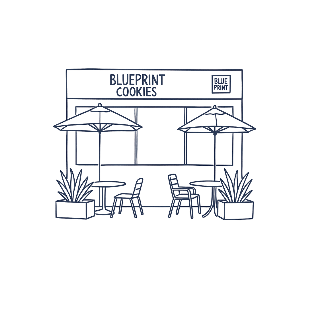 Neon sign outline of outdoor seating area with tables, chairs, umbrellas, and potted plants in front of a bakery sign that reads 'Blueprint Cookies'.