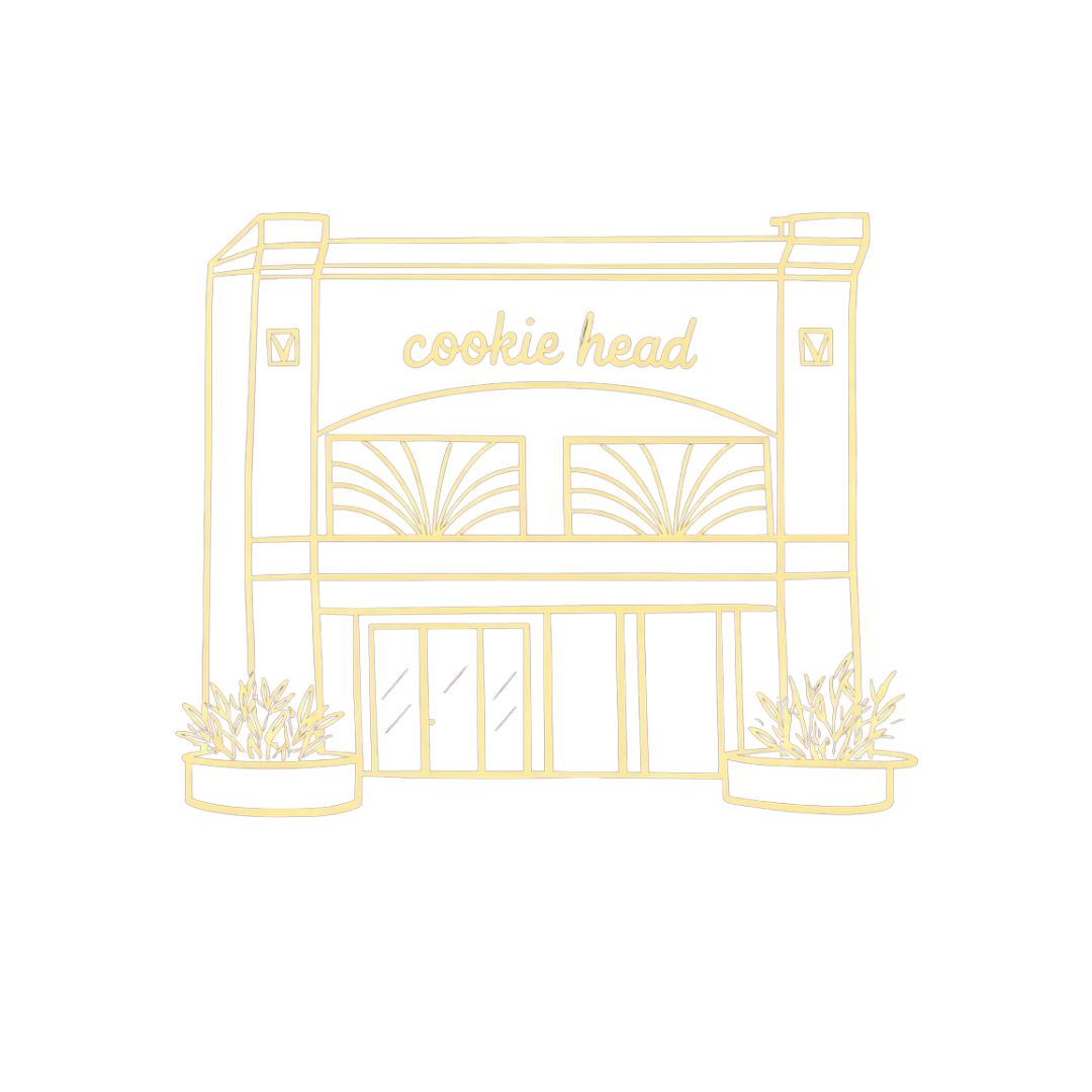 Neon sign of a bakery named Cookie Head with decorative plants outside on a black background.