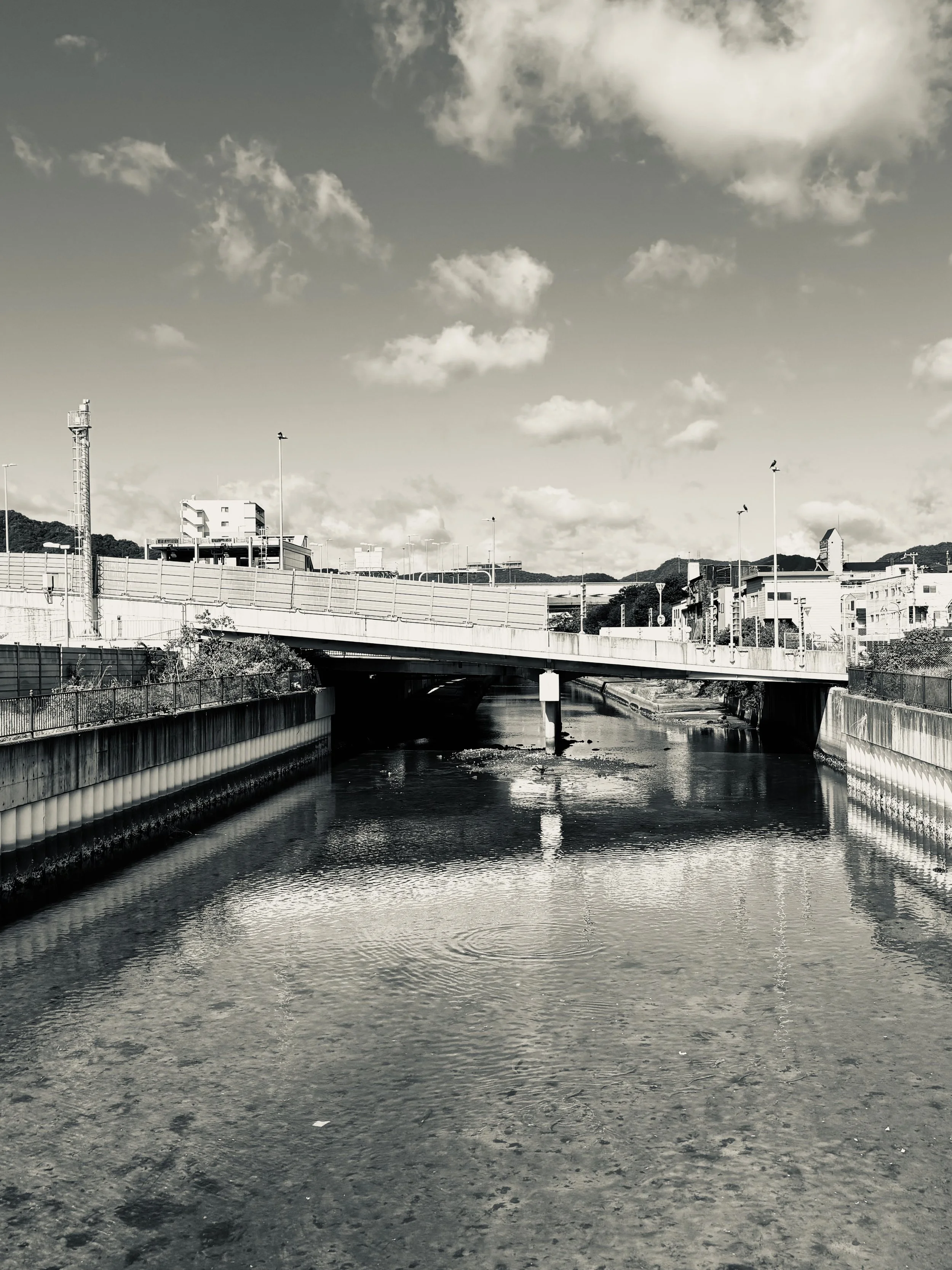Minato River in Shin-Nagata, Kobe, Japan, shown in black and white with bridge and reflections, evoking stillness, flow, and urban landscape