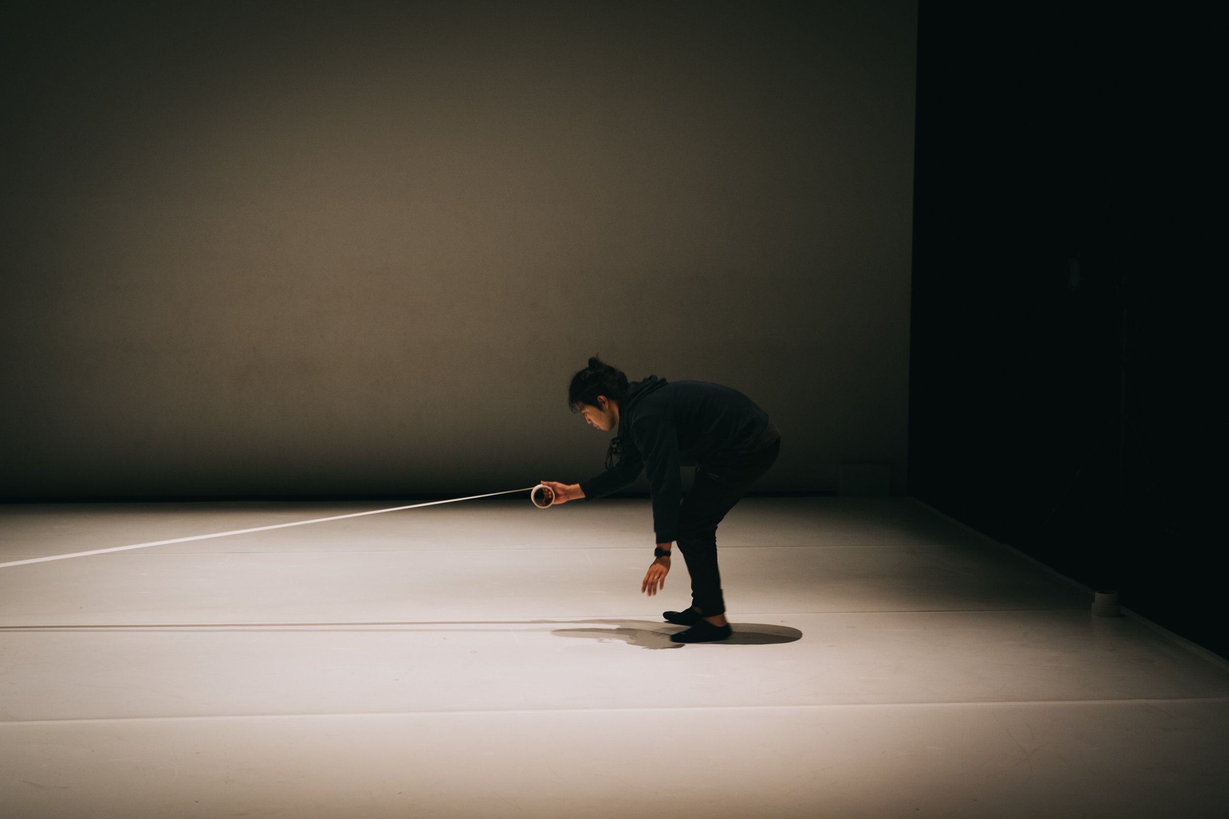 One stage crew laying a tape line across the stage in Total Beings | Burning Hearts.