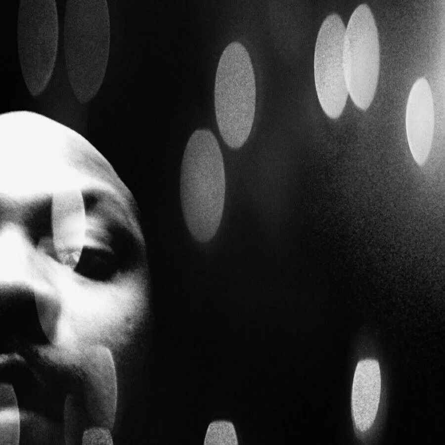 Close-up abstract black and white portrait of J’Sun Howard with blurred motion and soft light orbs, evoking memory and ephemeral presence