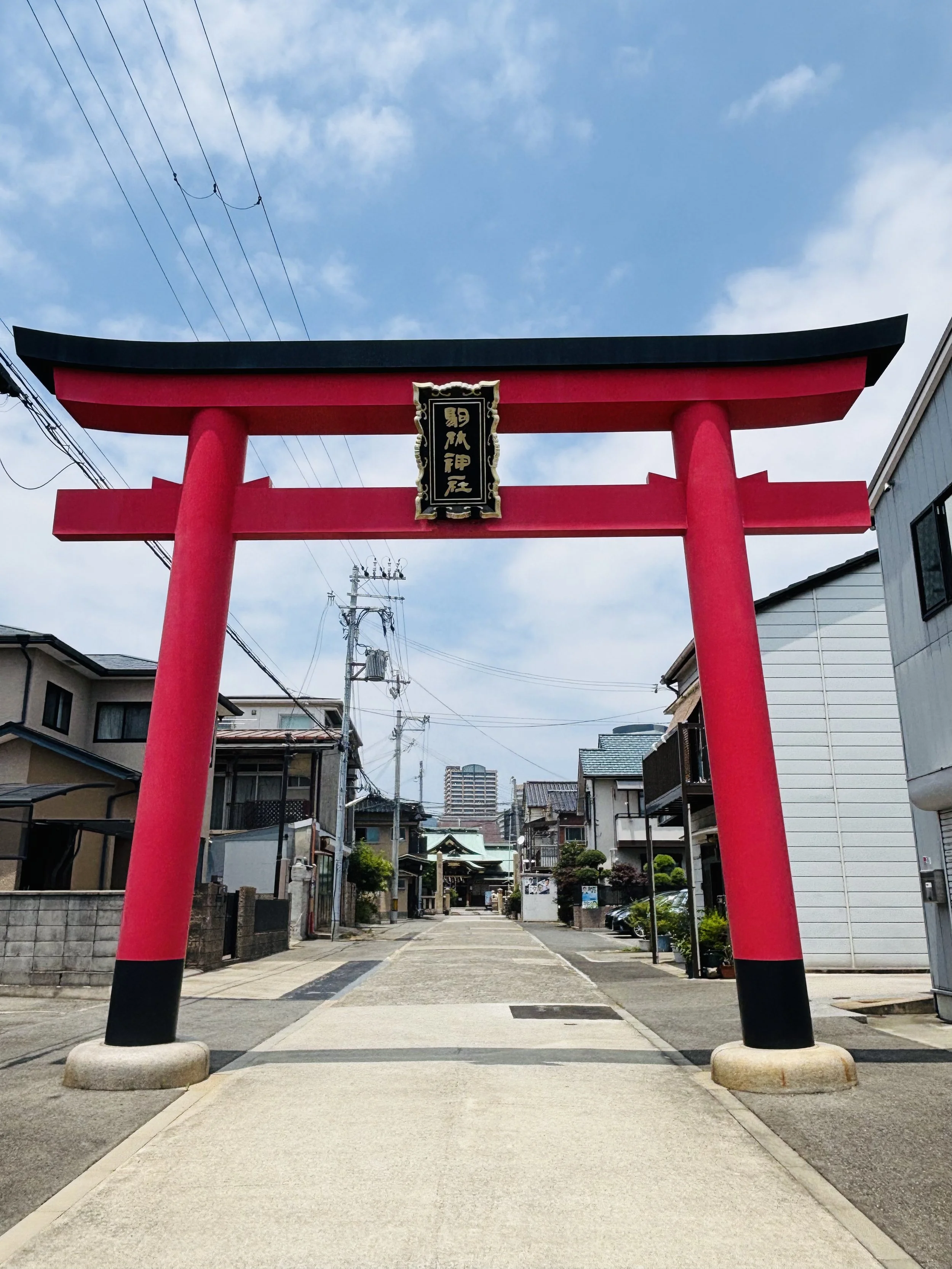 Torii gate entrance to Komagabayashi Shrine in Kobe, Japan, framing a neighborhood street and marking a threshold into sacred space