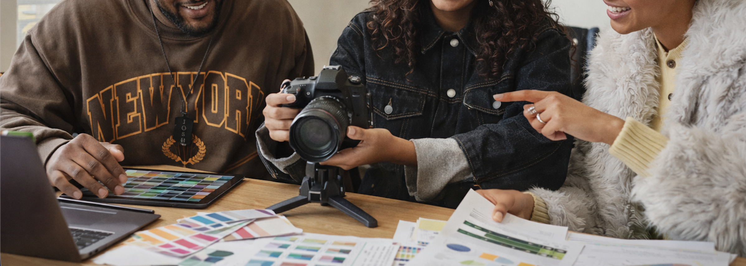 Three people examining a camera and color samples on a table, involved in a creative or design project.